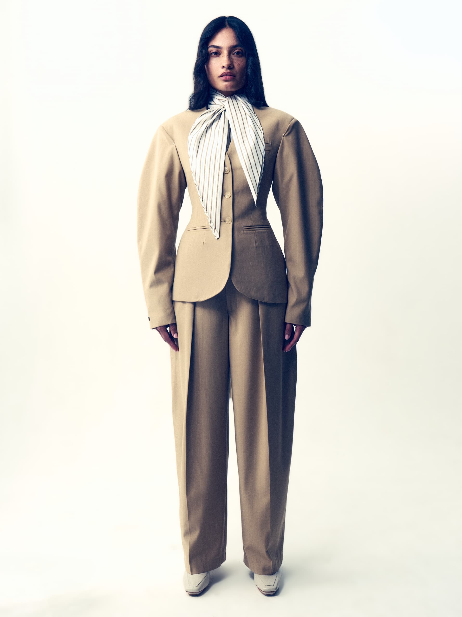 Fashion model in tailored beige suit and striped scarf, minimalist style.
