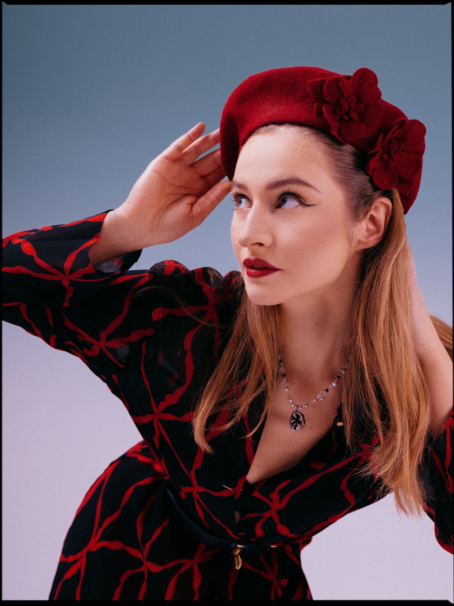 Woman in red beret and dress, striking pose against blue background. Fashionable look.