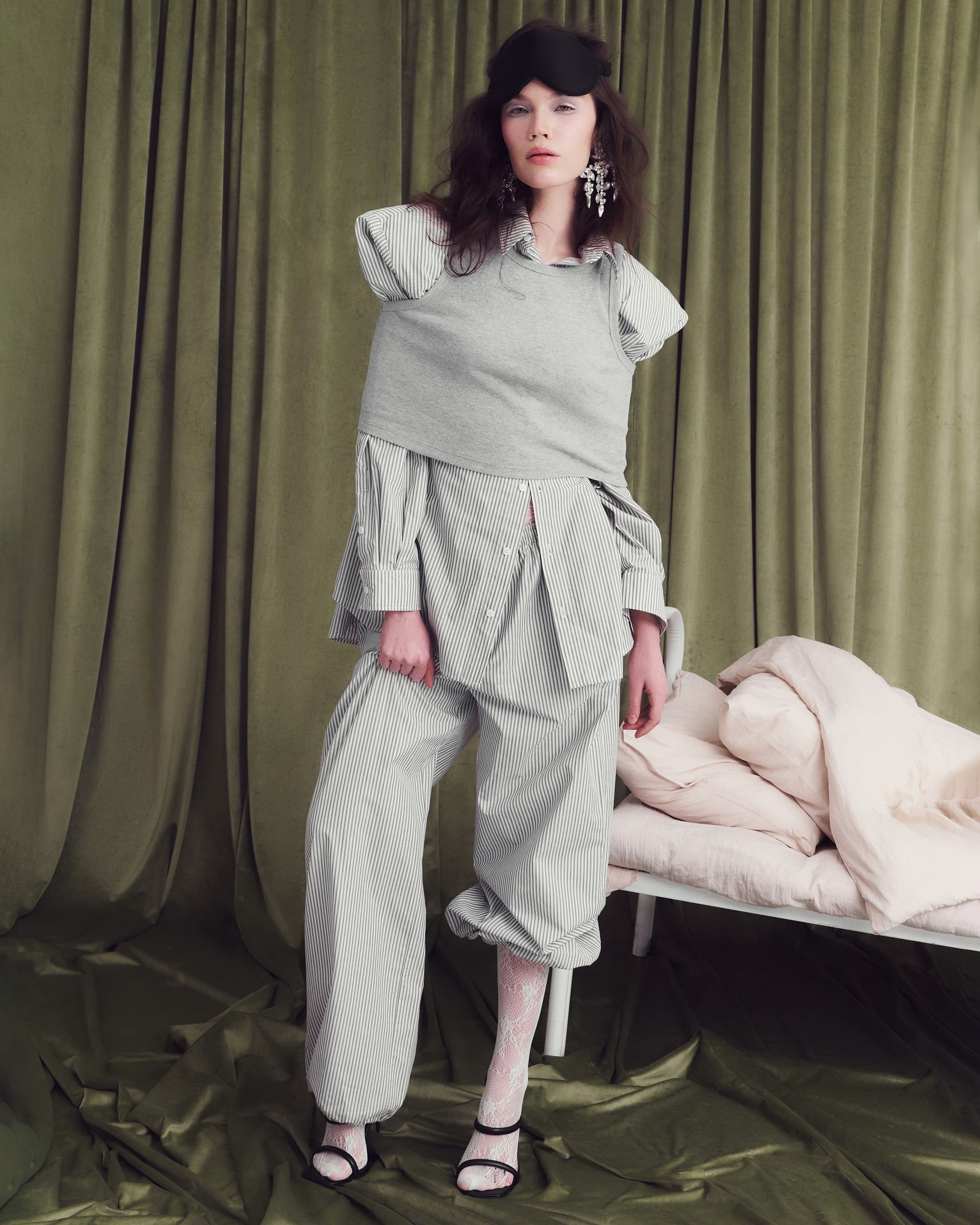 Fashionable woman in layered outfit with eye mask, posing in a stylish room.