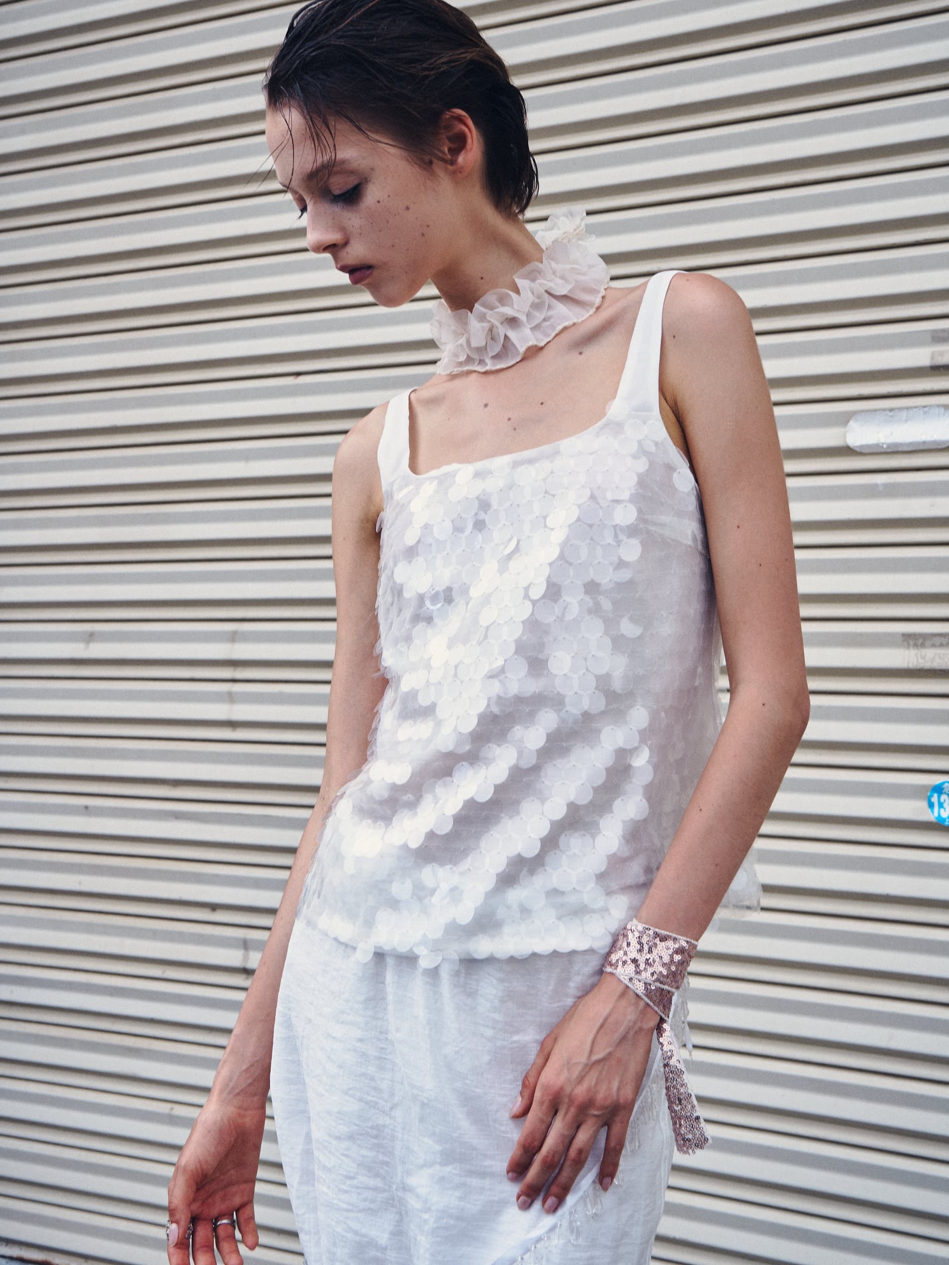 Fashion model in white sequin top poses against striped metal background.