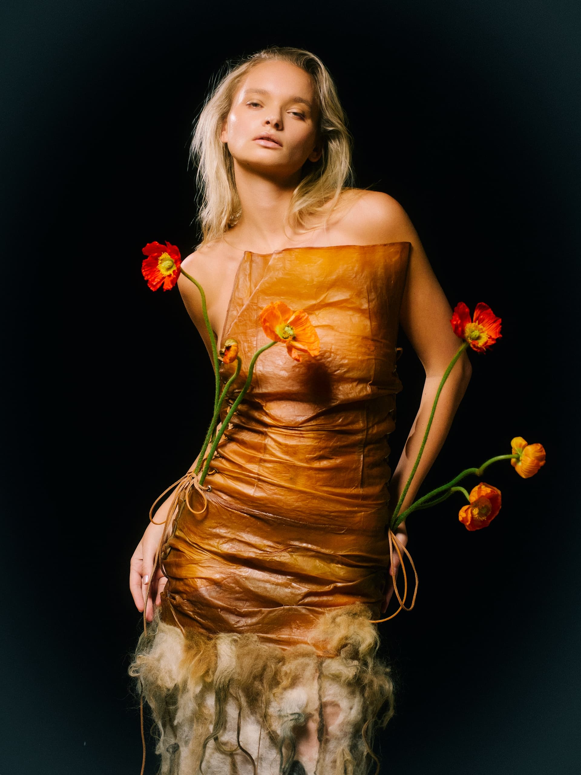 Woman in an orange artistic dress with bright flowers on a black background.