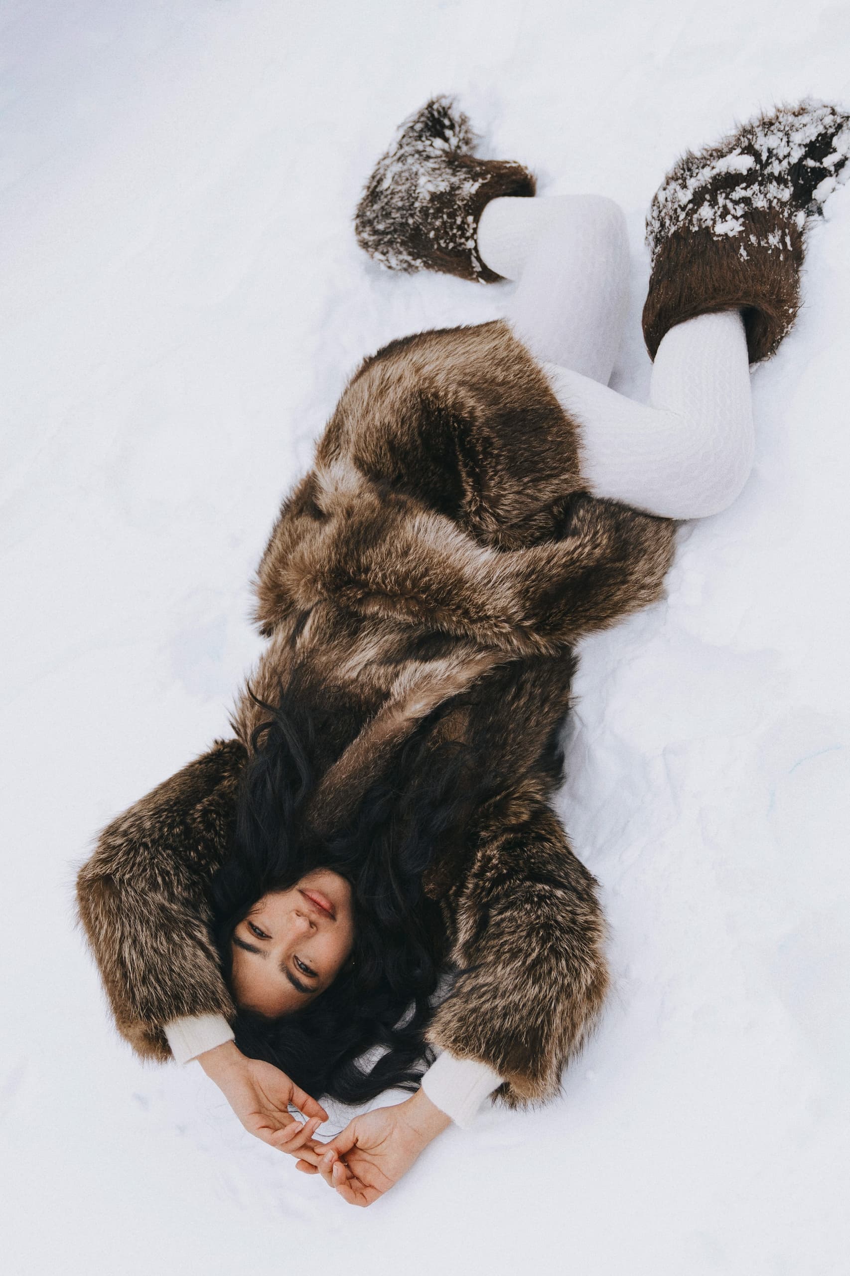 Woman in fur coat lying on snowy ground, embracing winter fashion.