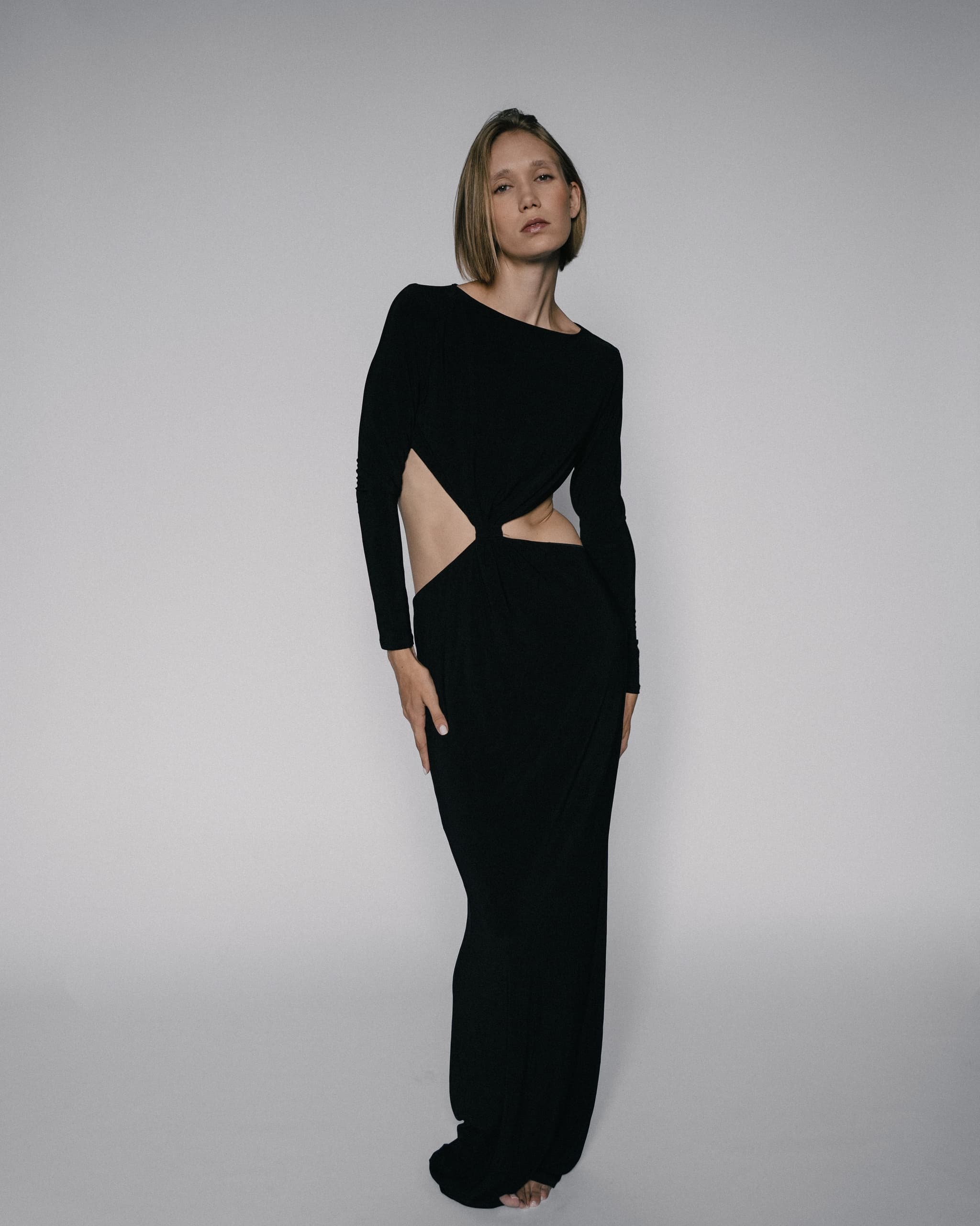 Woman in elegant black cutout gown poses against a minimalist background.