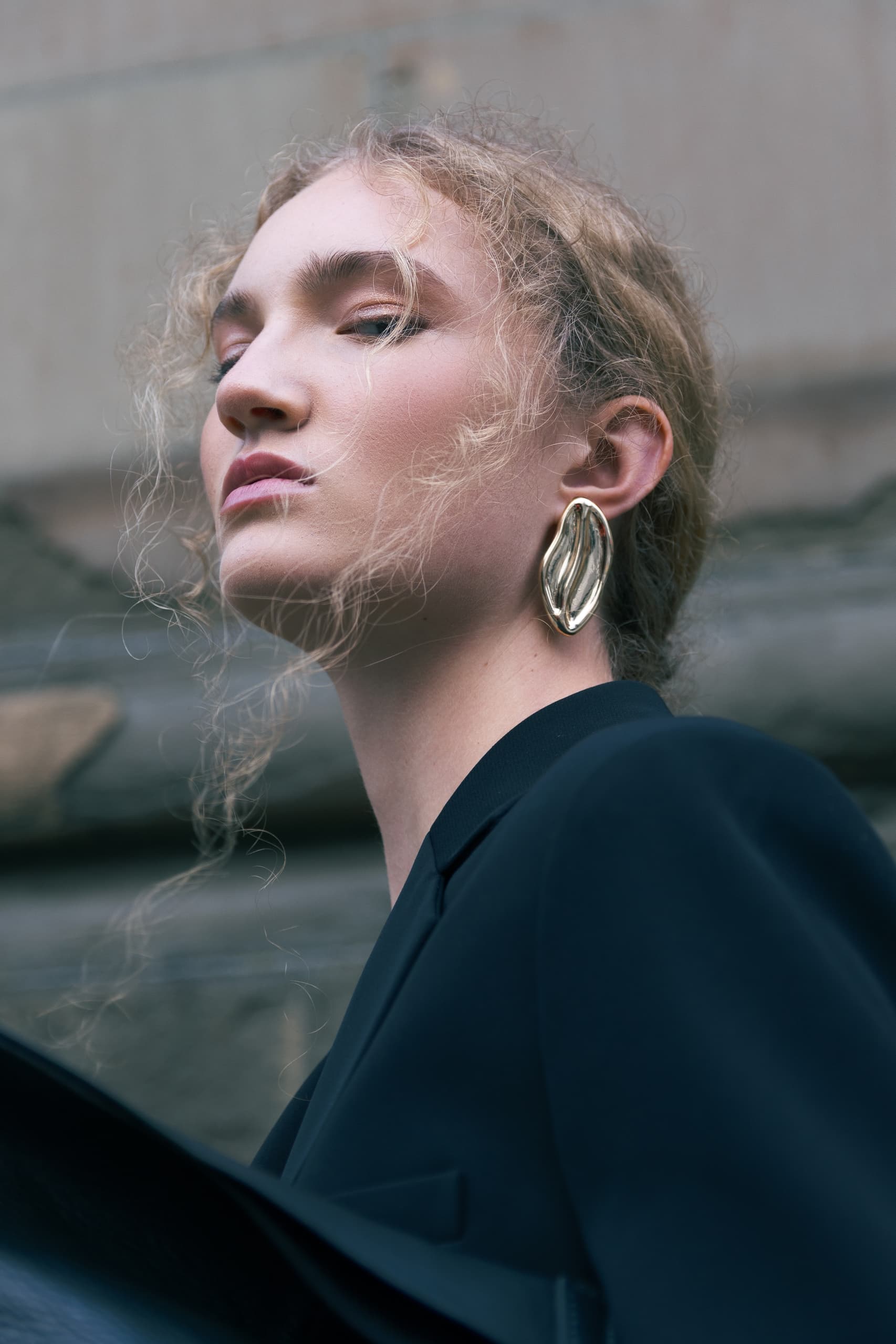Elegant woman in black outfit with bold gold earrings, portrayed from a low angle.