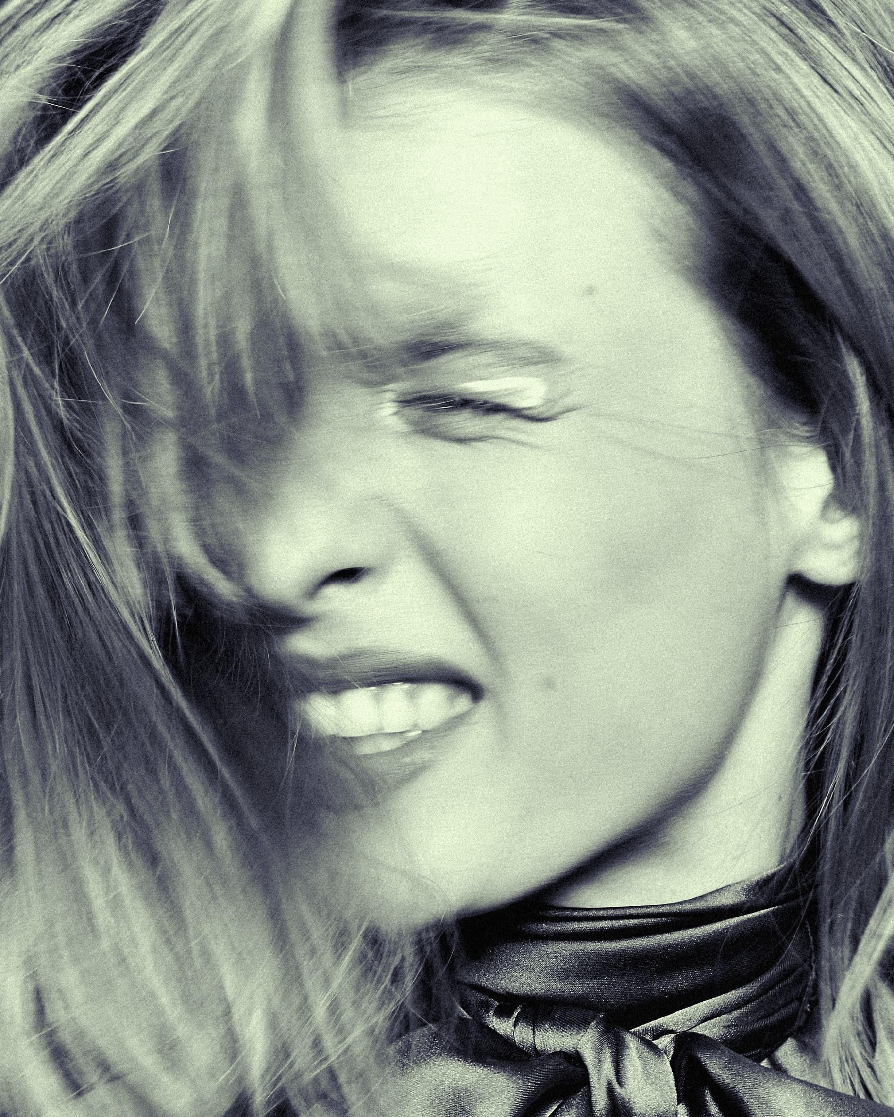Woman smiling and moving hair, with a satin scarf; portrait in motion.