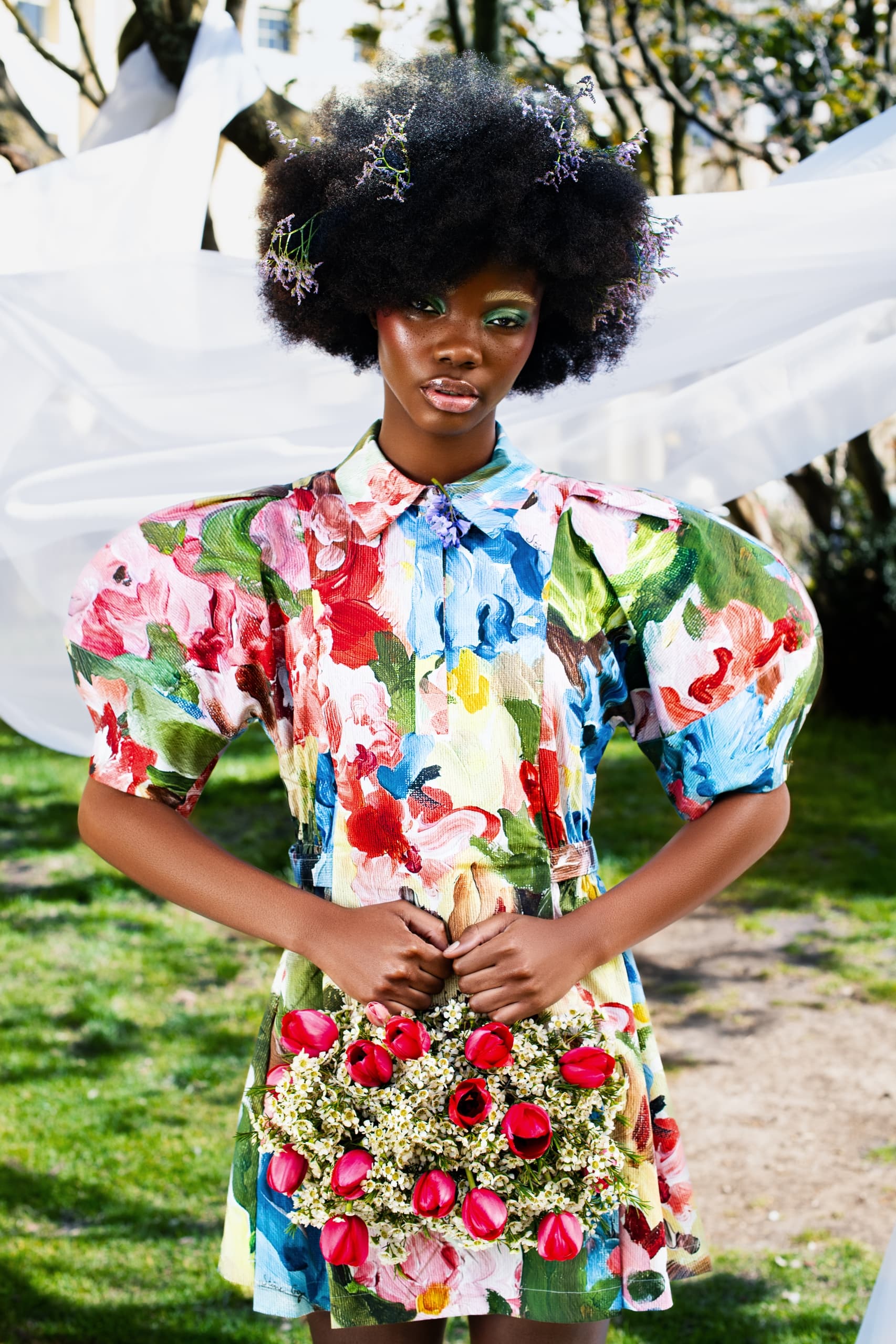 Woman in vibrant floral dress holding bouquet outdoors.