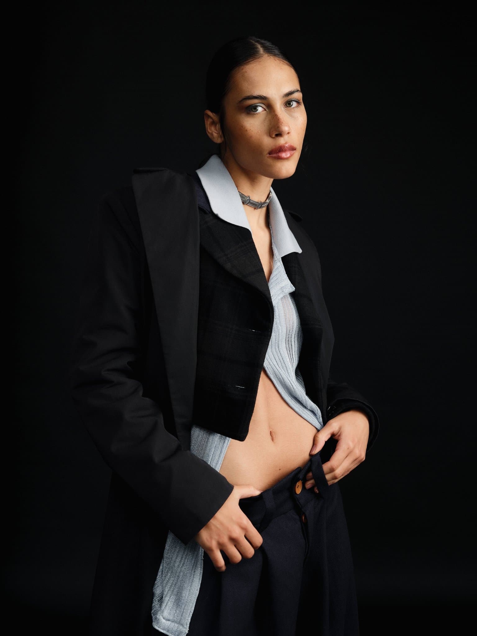 Fashionable woman in layered clothing against dark backdrop, showcasing modern style.