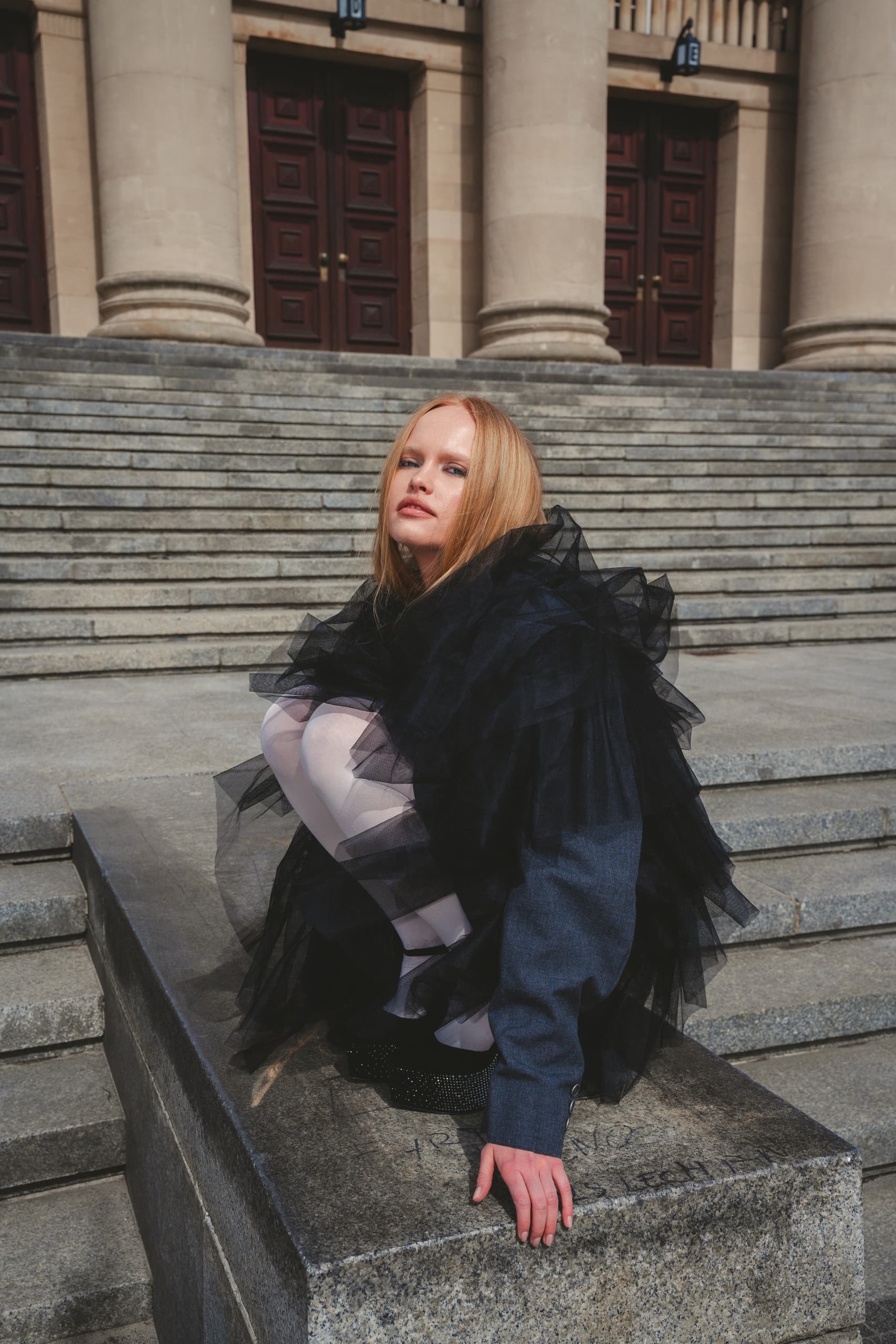 Fashionable woman in tulle outfit poses on stone steps.