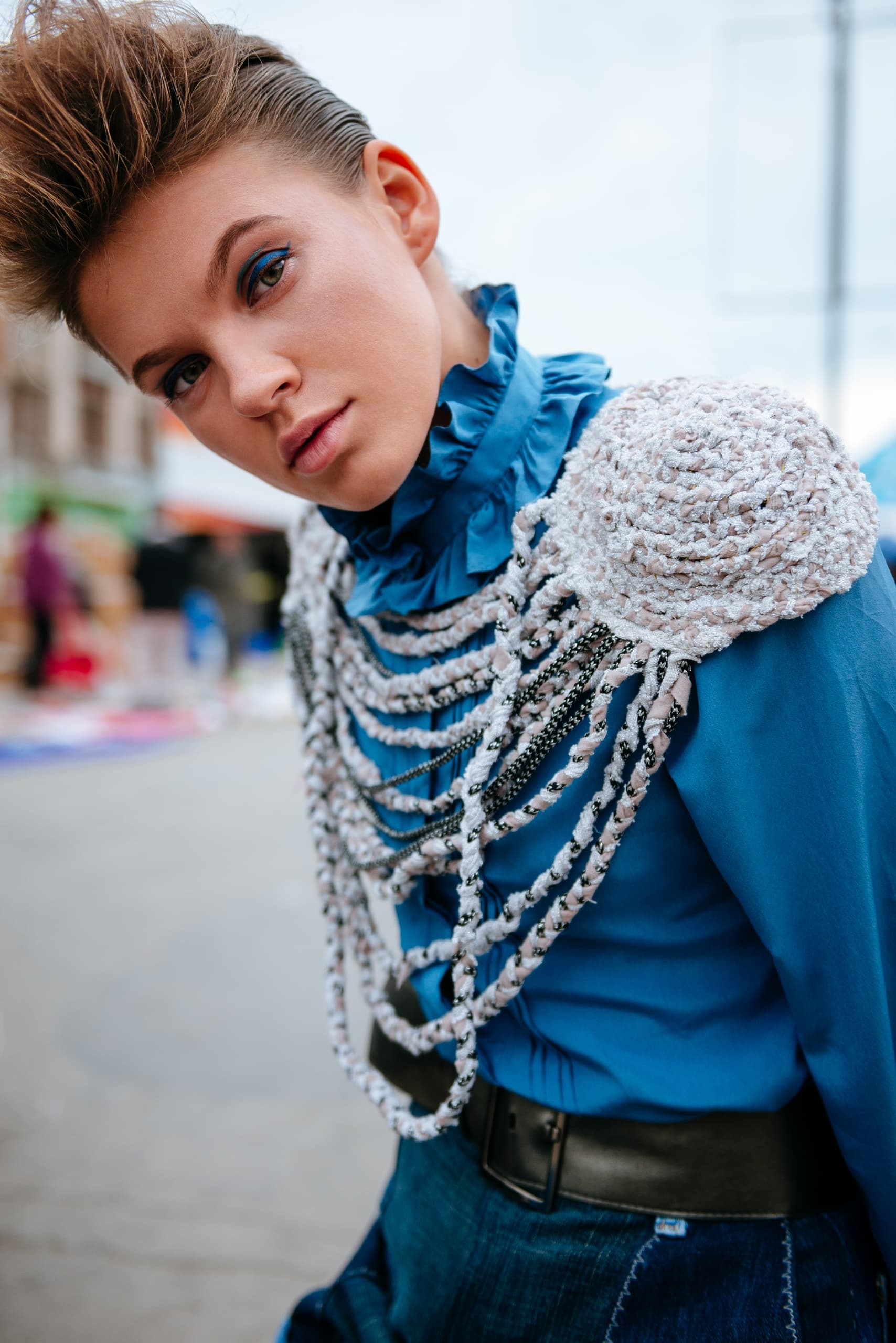 Fashionable individual in a blue outfit with unique shoulder detailing.