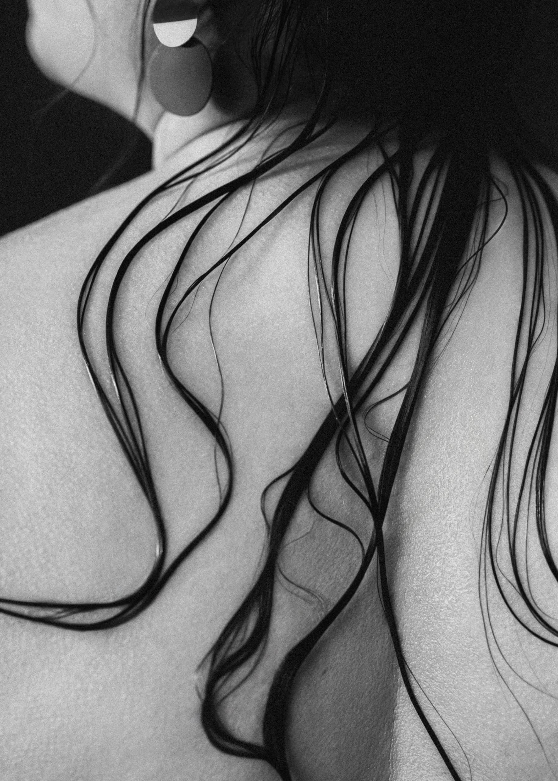 Close-up of wet hair cascading over a woman's bare back in black and white.