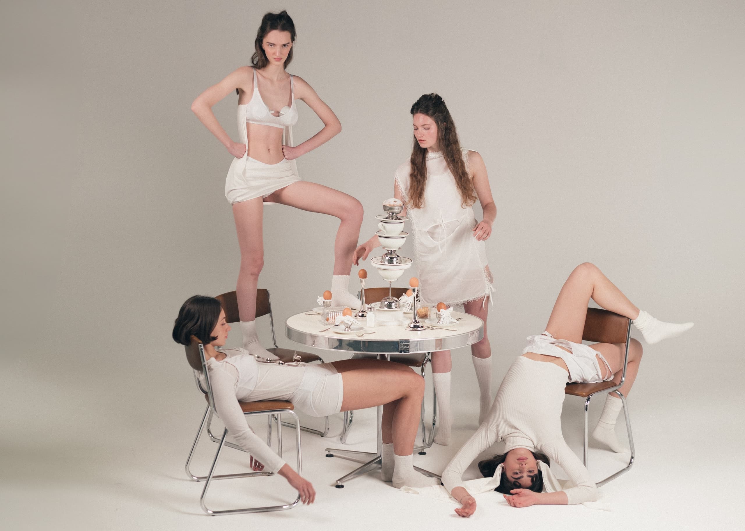 Women in white fashion posing with breakfast table setup, modern aesthetic.