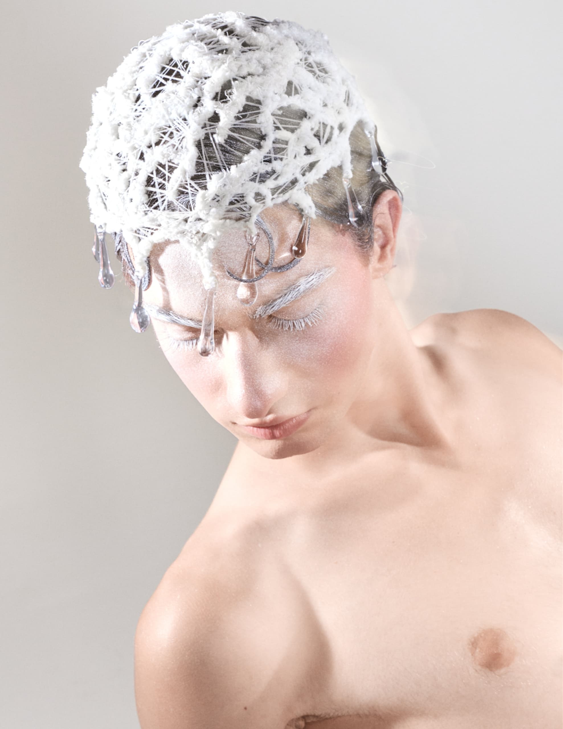 Avant-garde fashion with a white net headpiece and artistic makeup.