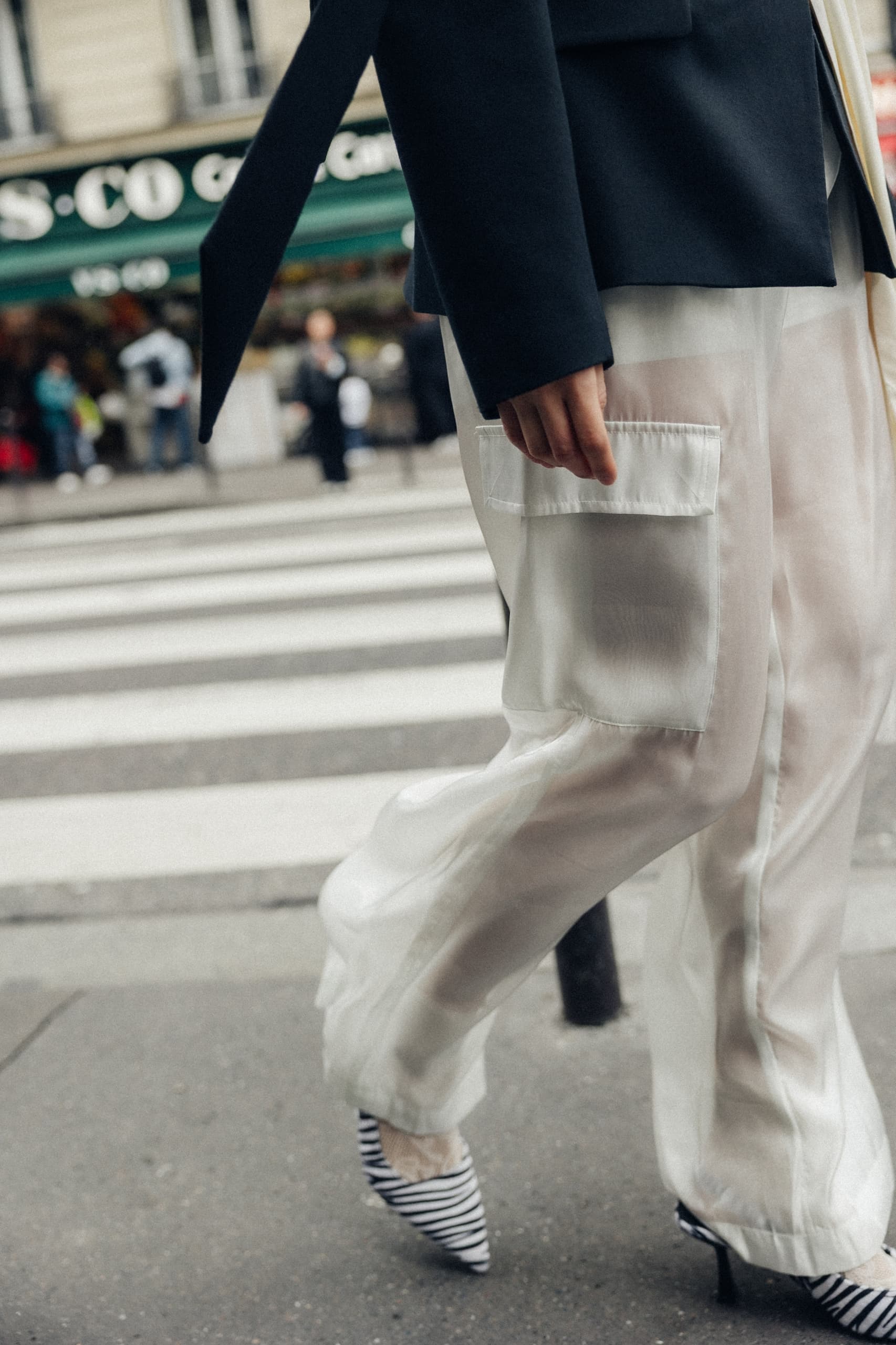 Chic urban fashion: Woman in sheer pants and striped heels crossing street.
