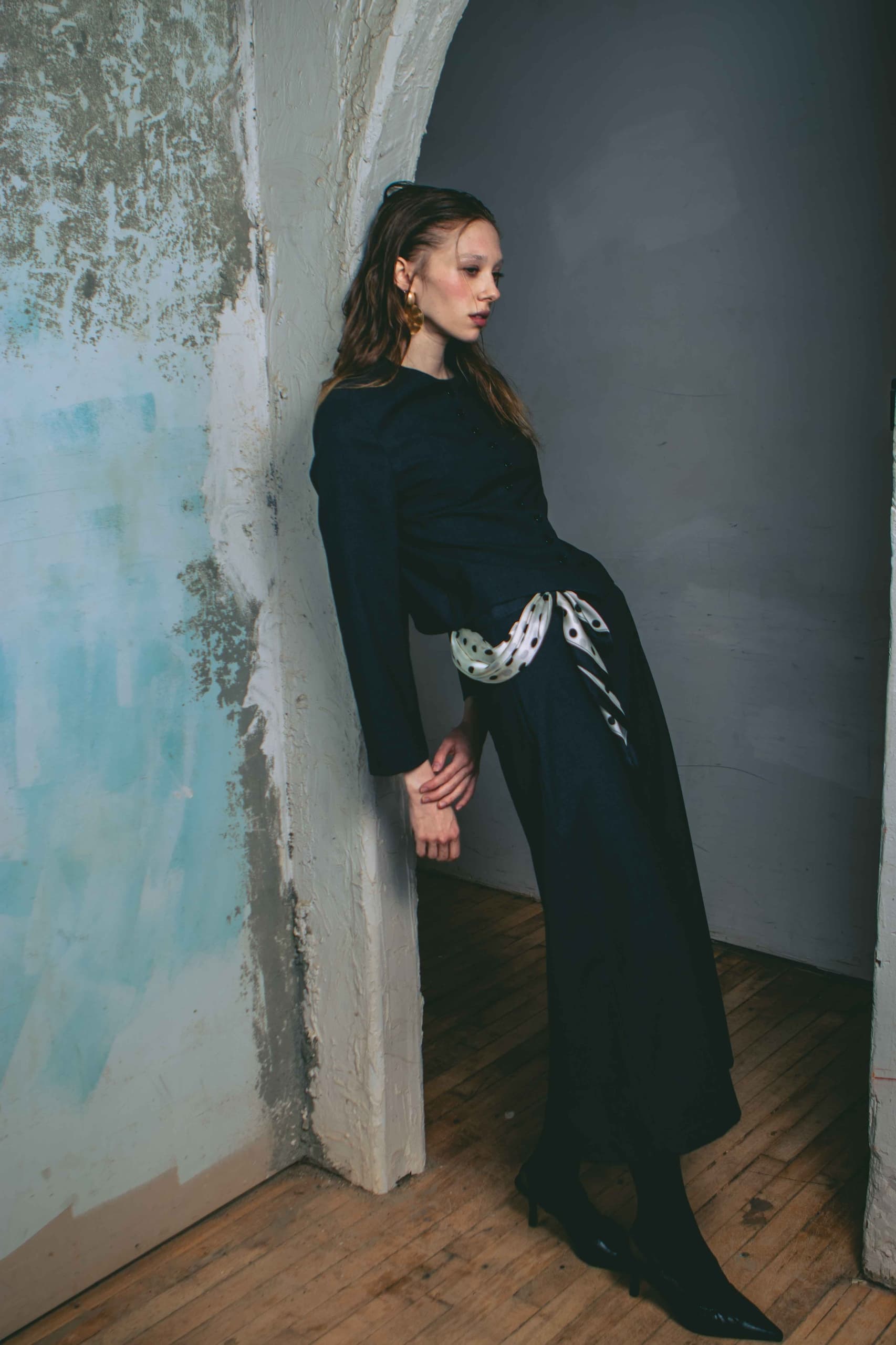 Fashion model in black dress leaning against an artistic wall.