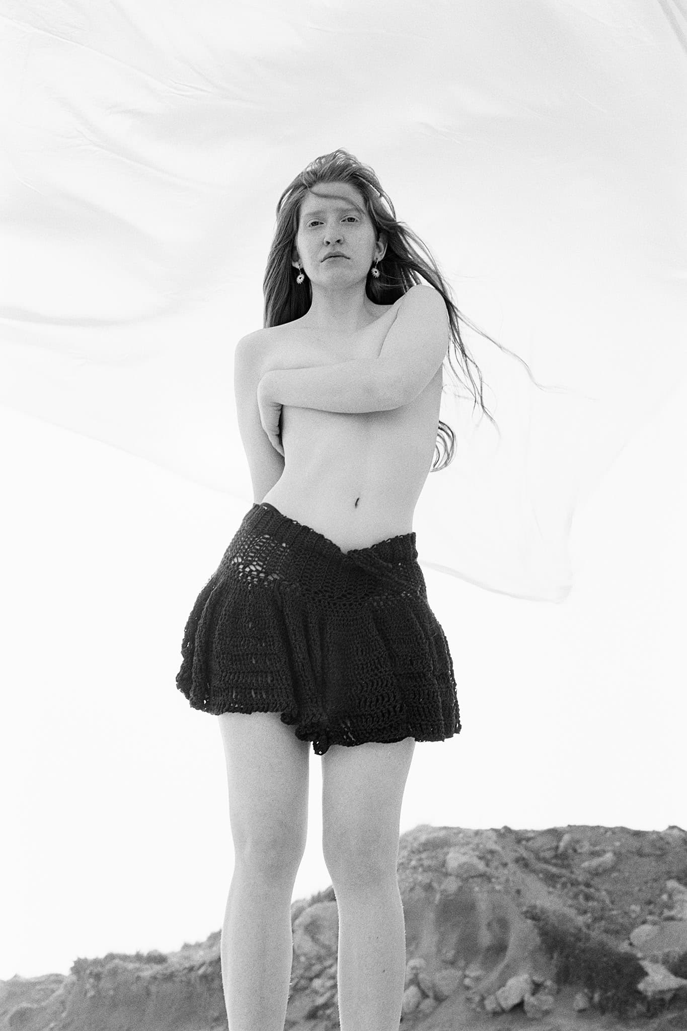 Person in a black crochet skirt against a white background, outdoors on a rocky terrain.