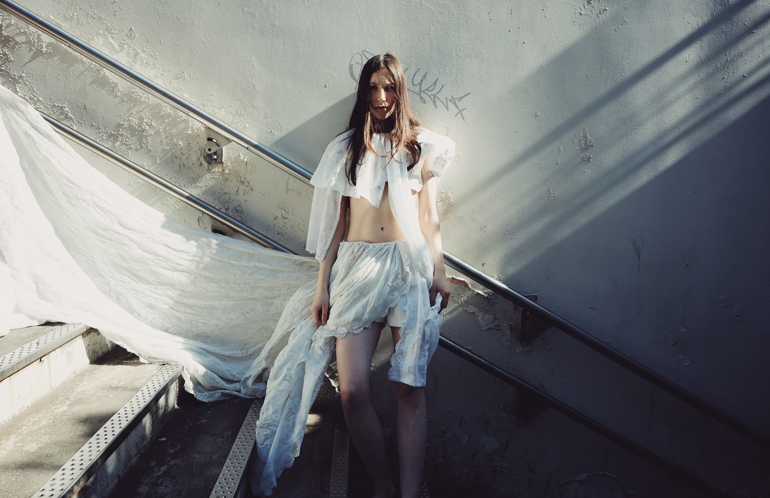 Woman in white dress standing on stairs in sunlight.