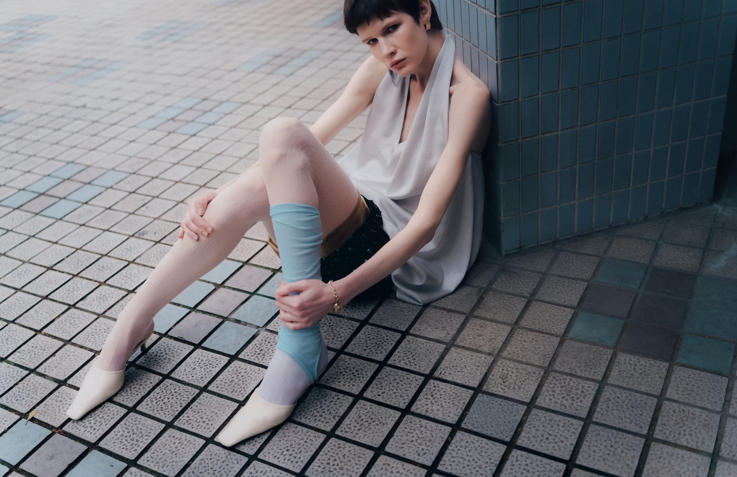 Fashion model in chic outfit sits on tiled floor, striking a stylish pose.