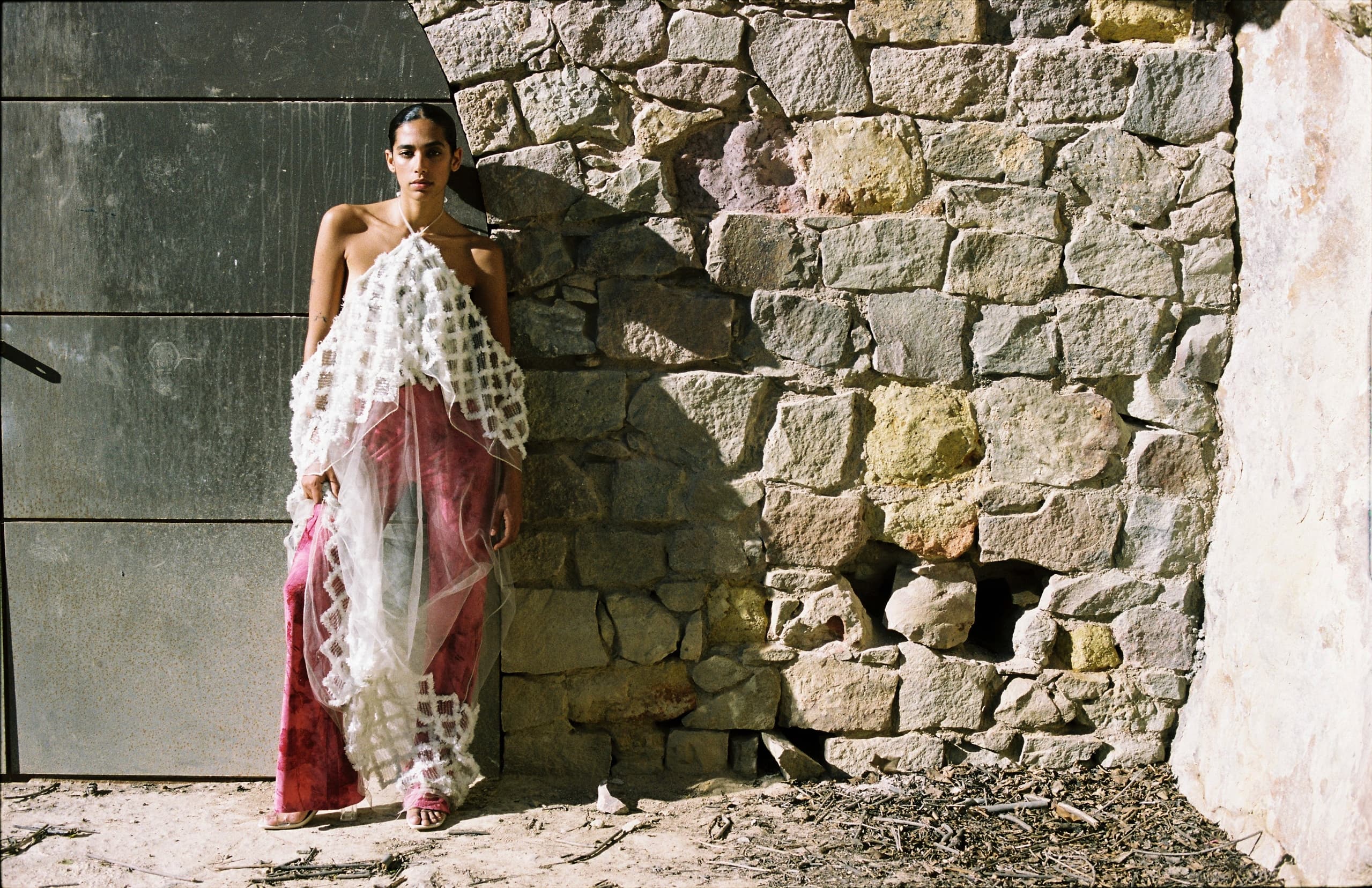 Fashion model in artistic outfit against rustic stone wall.