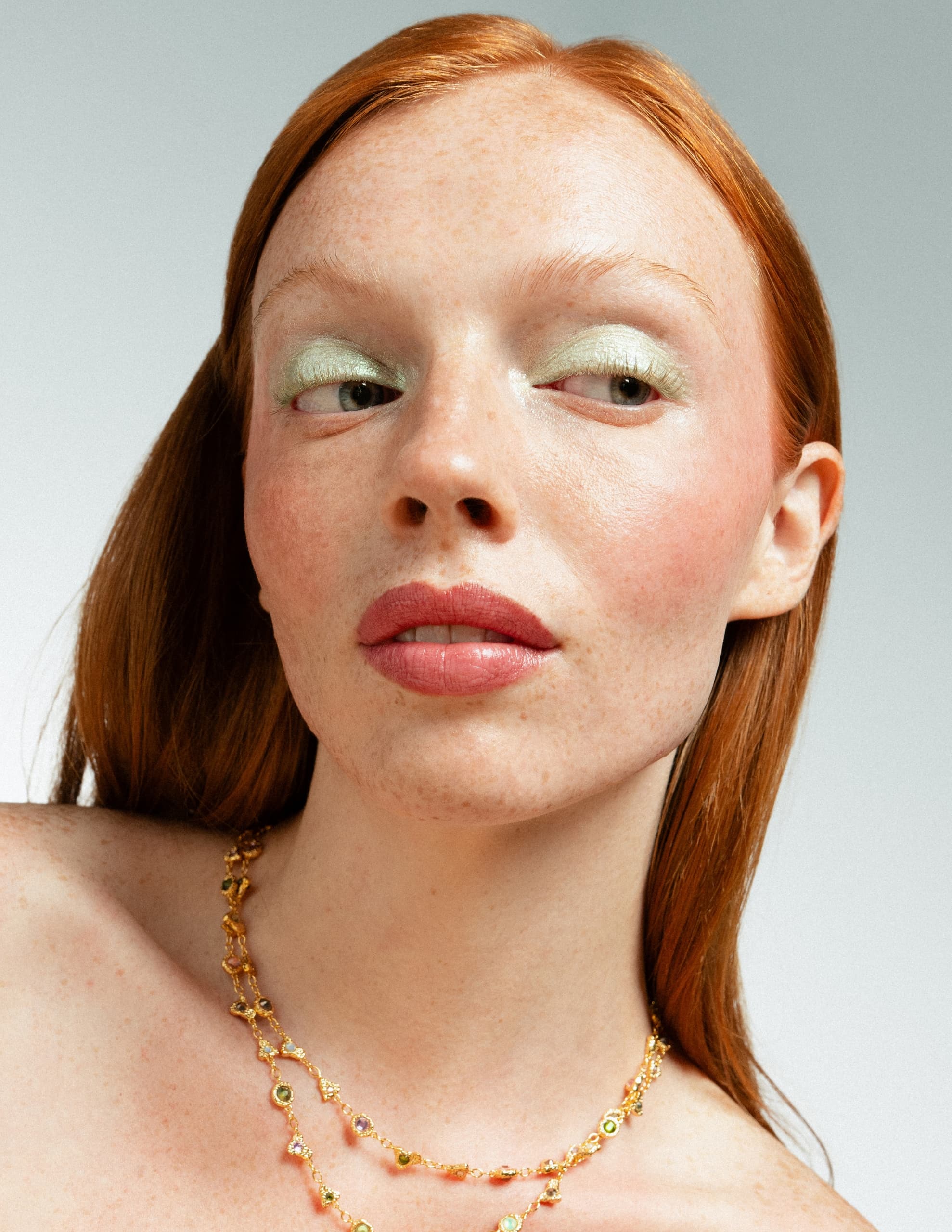 Red-haired woman with green eyeshadow and a gold necklace.