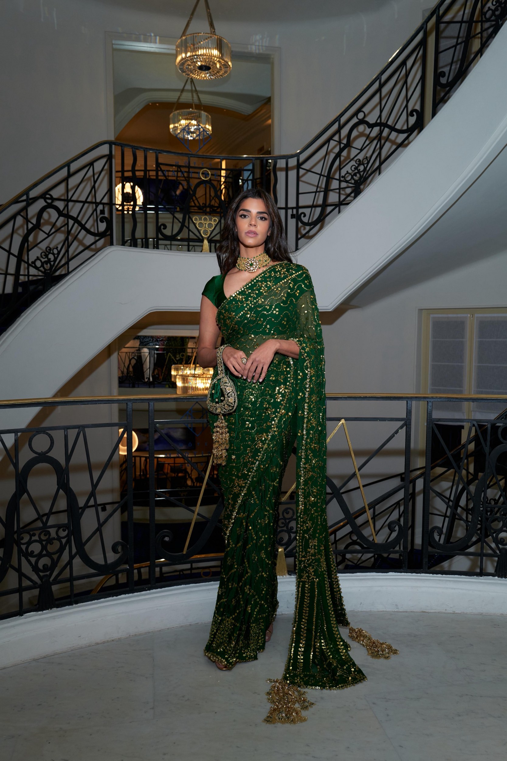 Elegant woman in green and gold saree on ornate staircase.