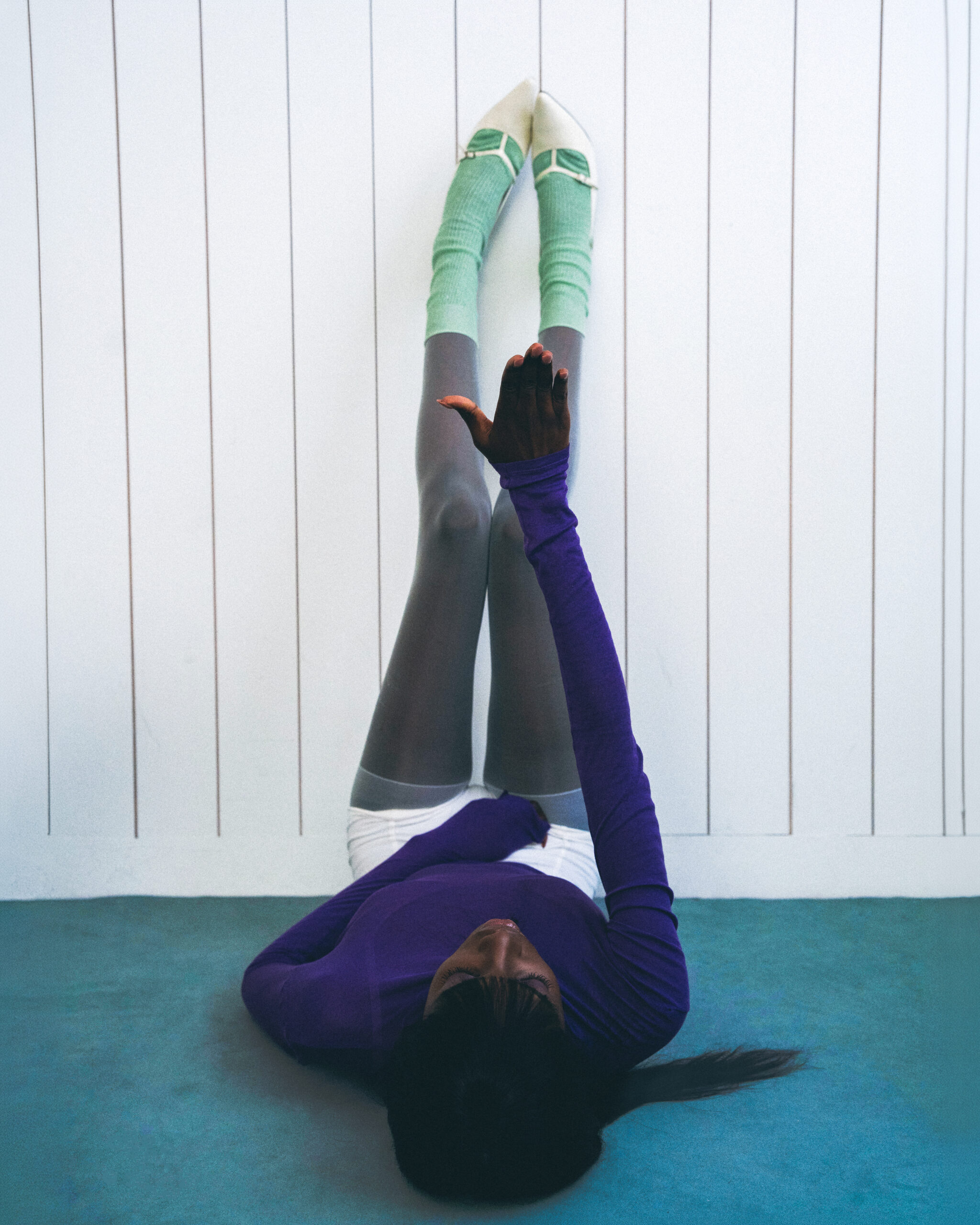 Person in vibrant socks and shoes lying against a wall with legs up.