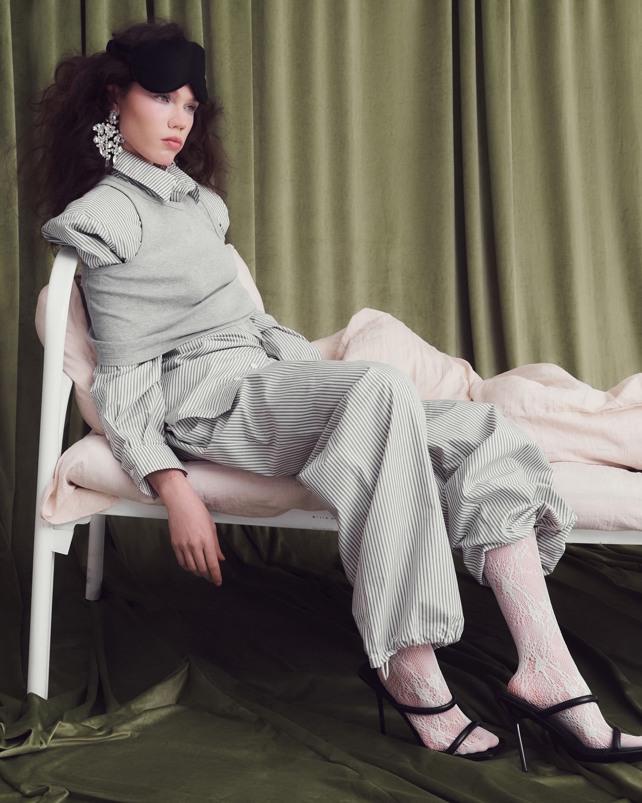 Woman in striped loungewear lounging on a chair against a green curtain backdrop.