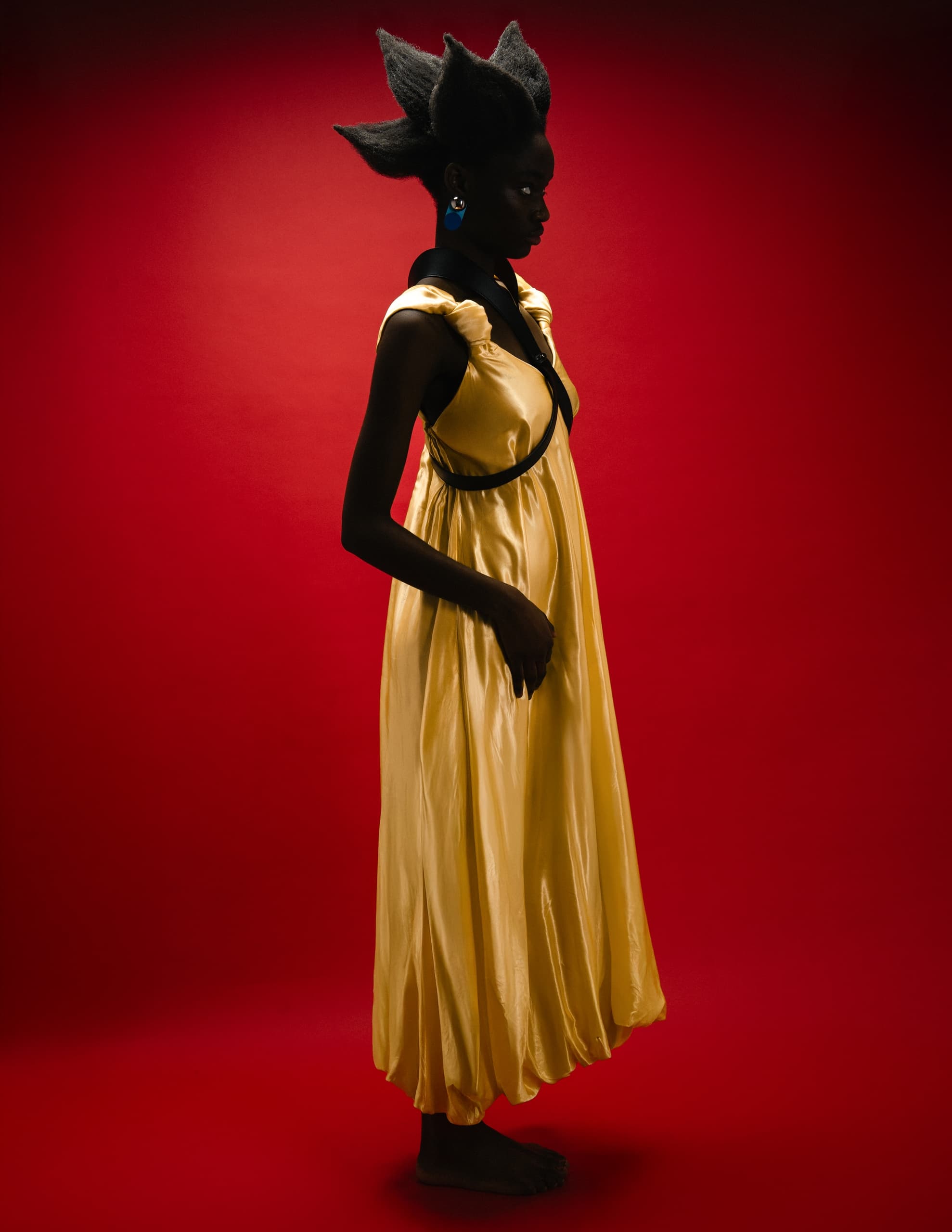 Fashion model in yellow dress with bold hairstyle on red background.