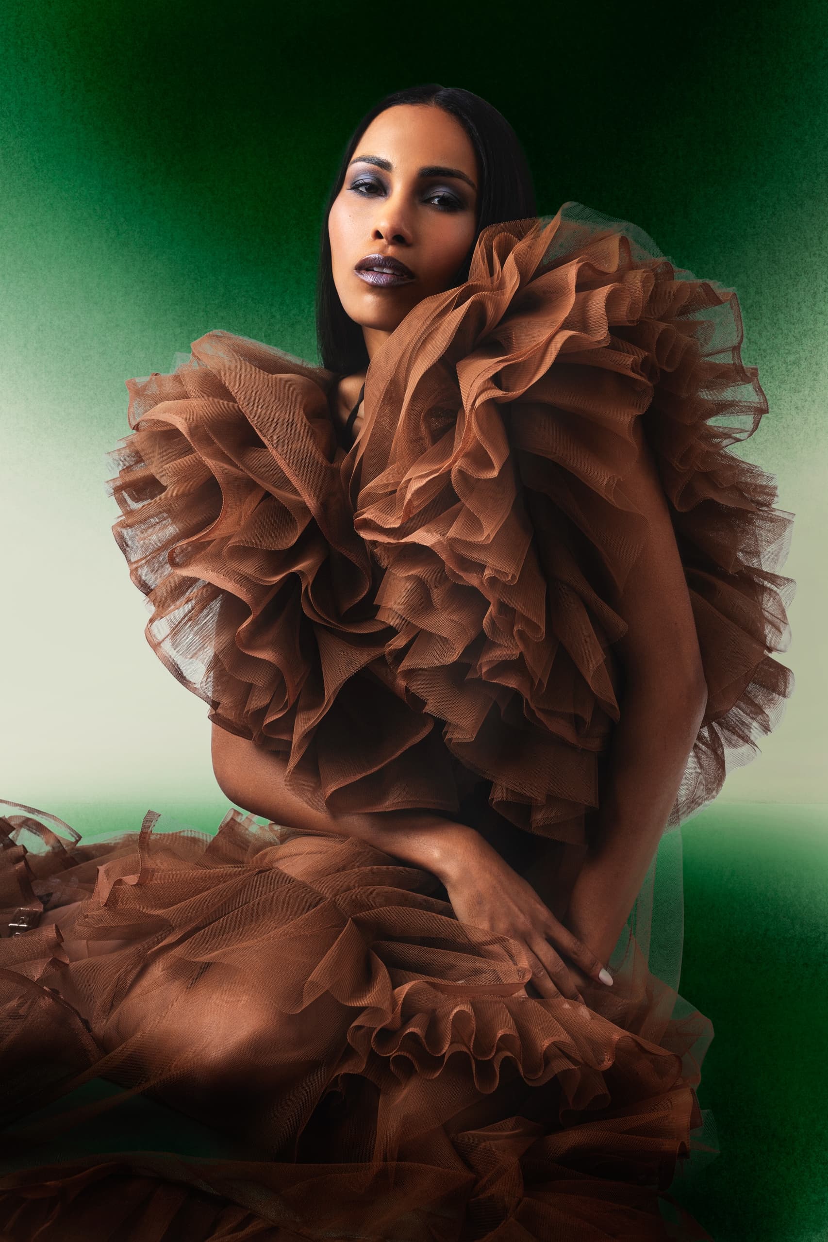 Elegant woman in ruffled brown dress against a green gradient backdrop. Fashion portrait.
