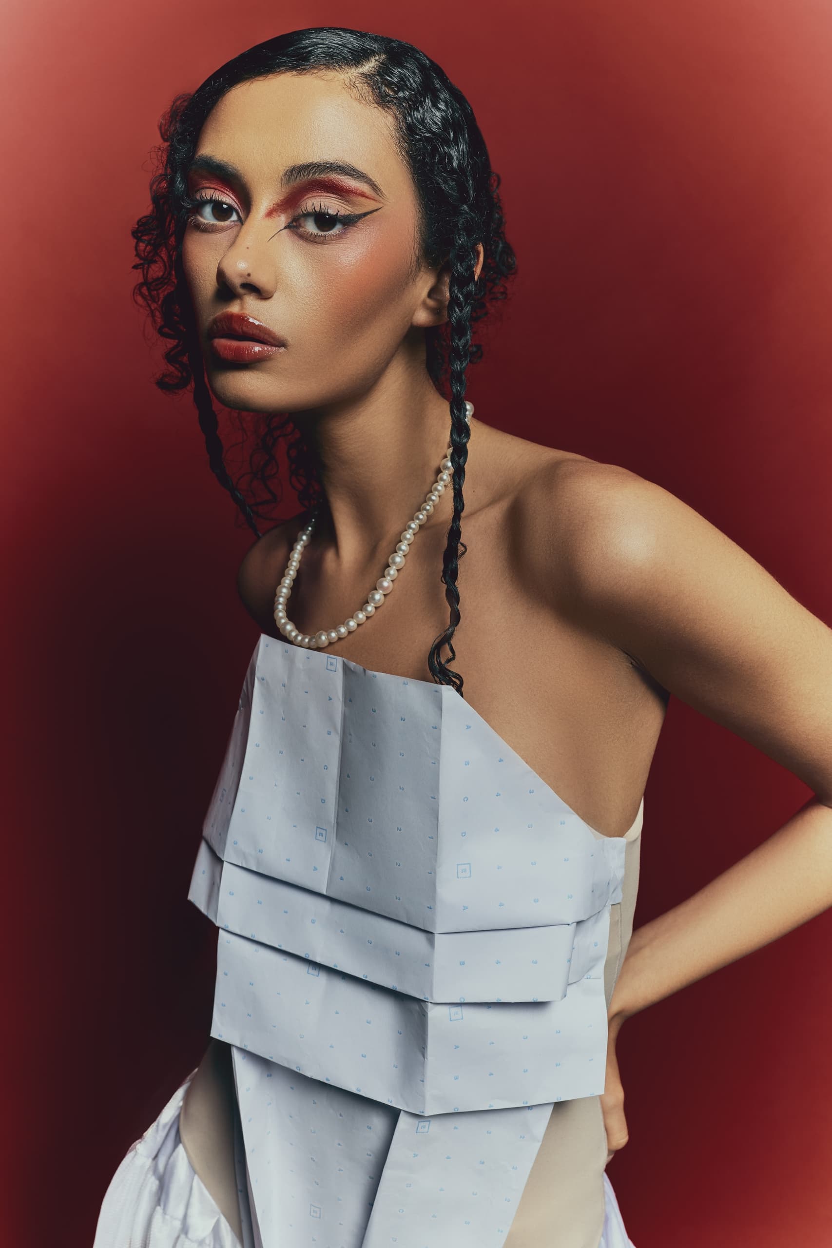 Stylish woman in edgy makeup and pearl necklace against red background.