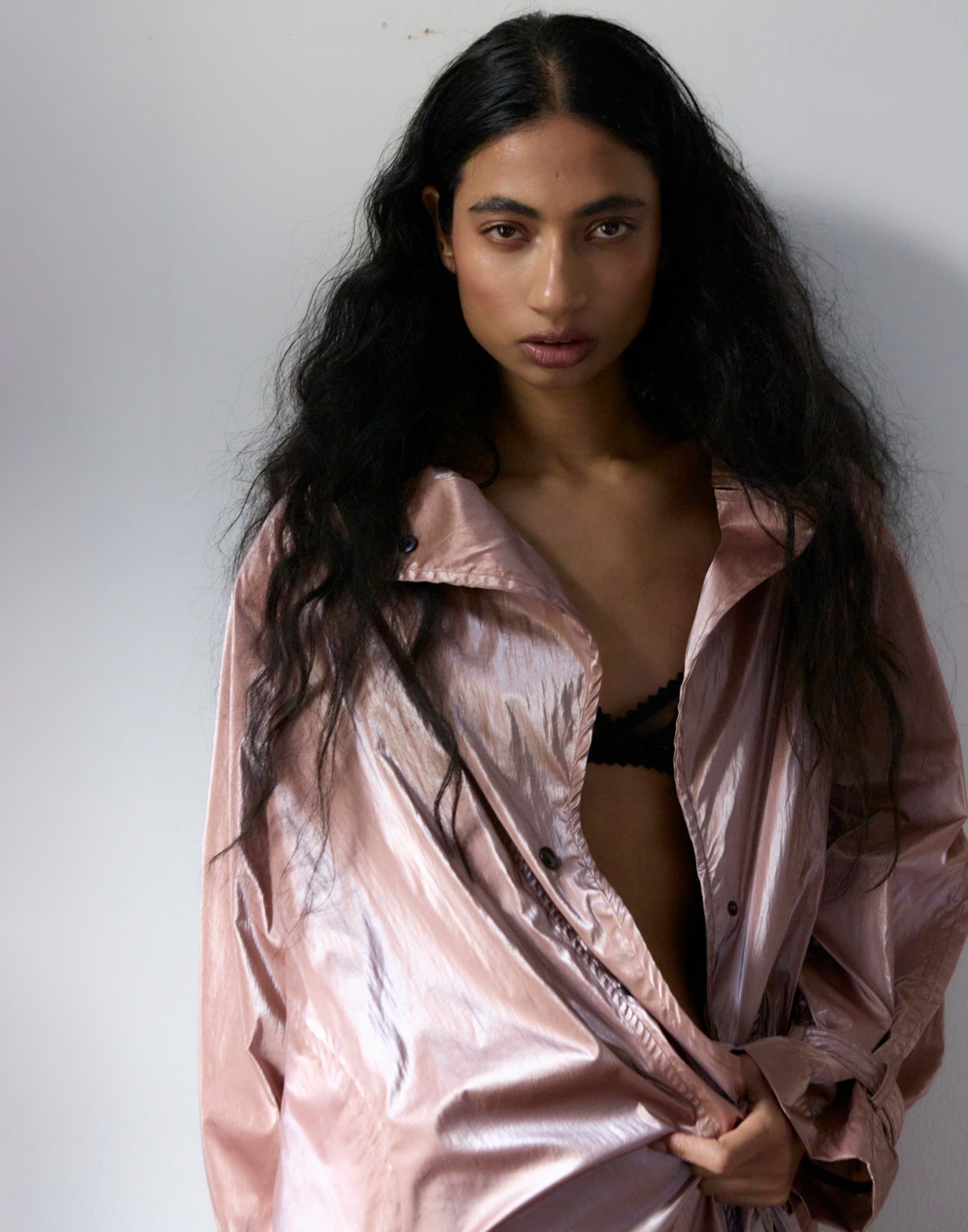 Woman in a shiny pink jacket with long hair, posing confidently against a white background.