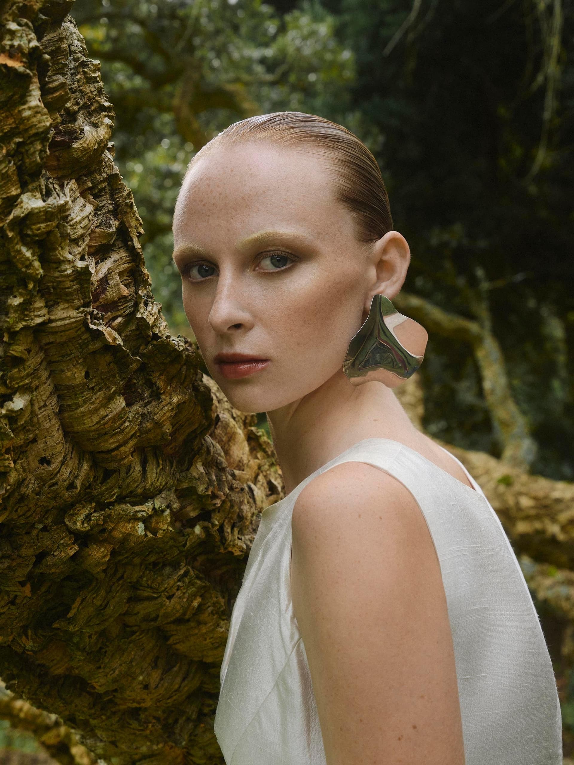 Woman in nature with slicked-back hair and large silver earring.