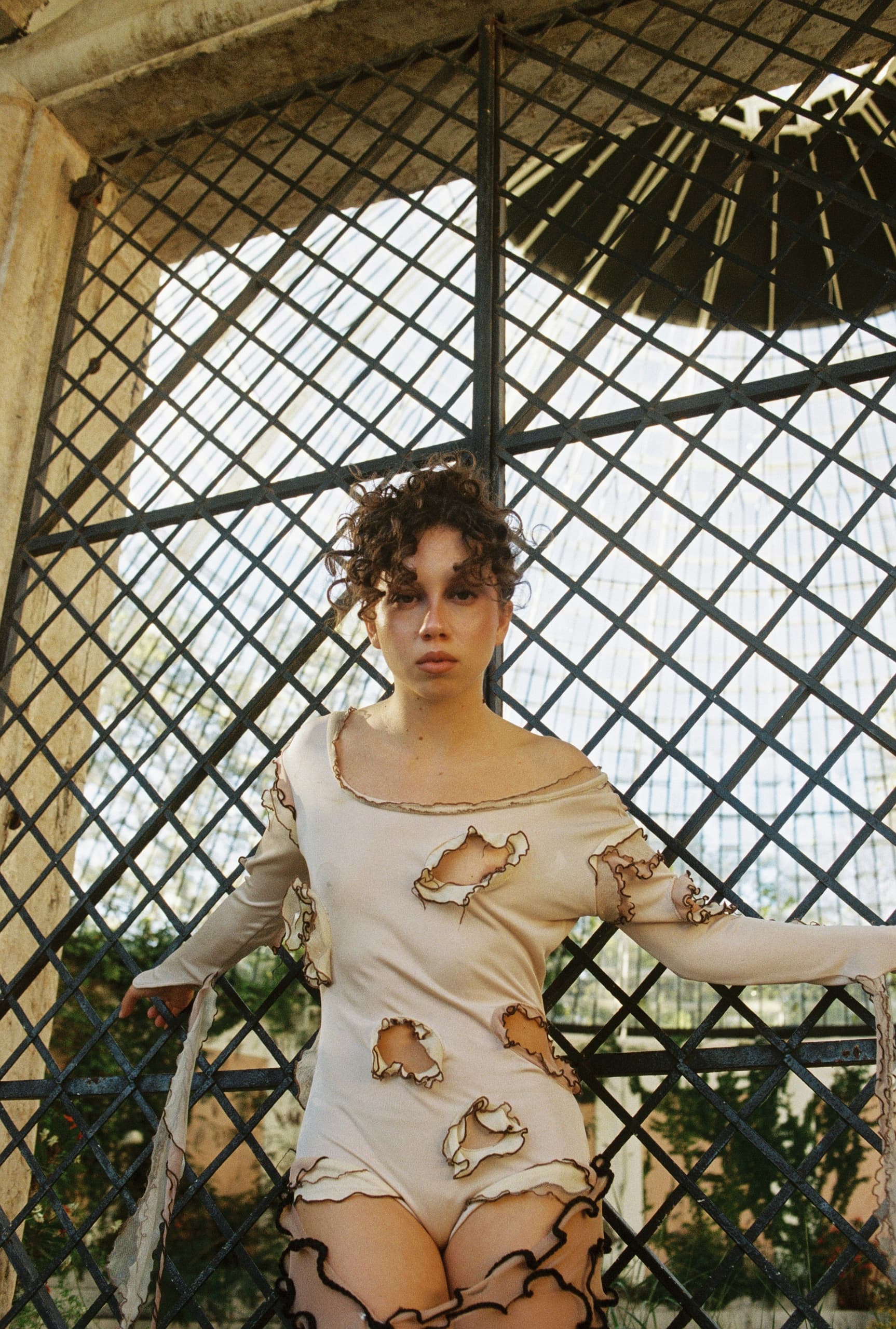 Person in fashion outfit with lattice backdrop, curly hair, artistic torn design.