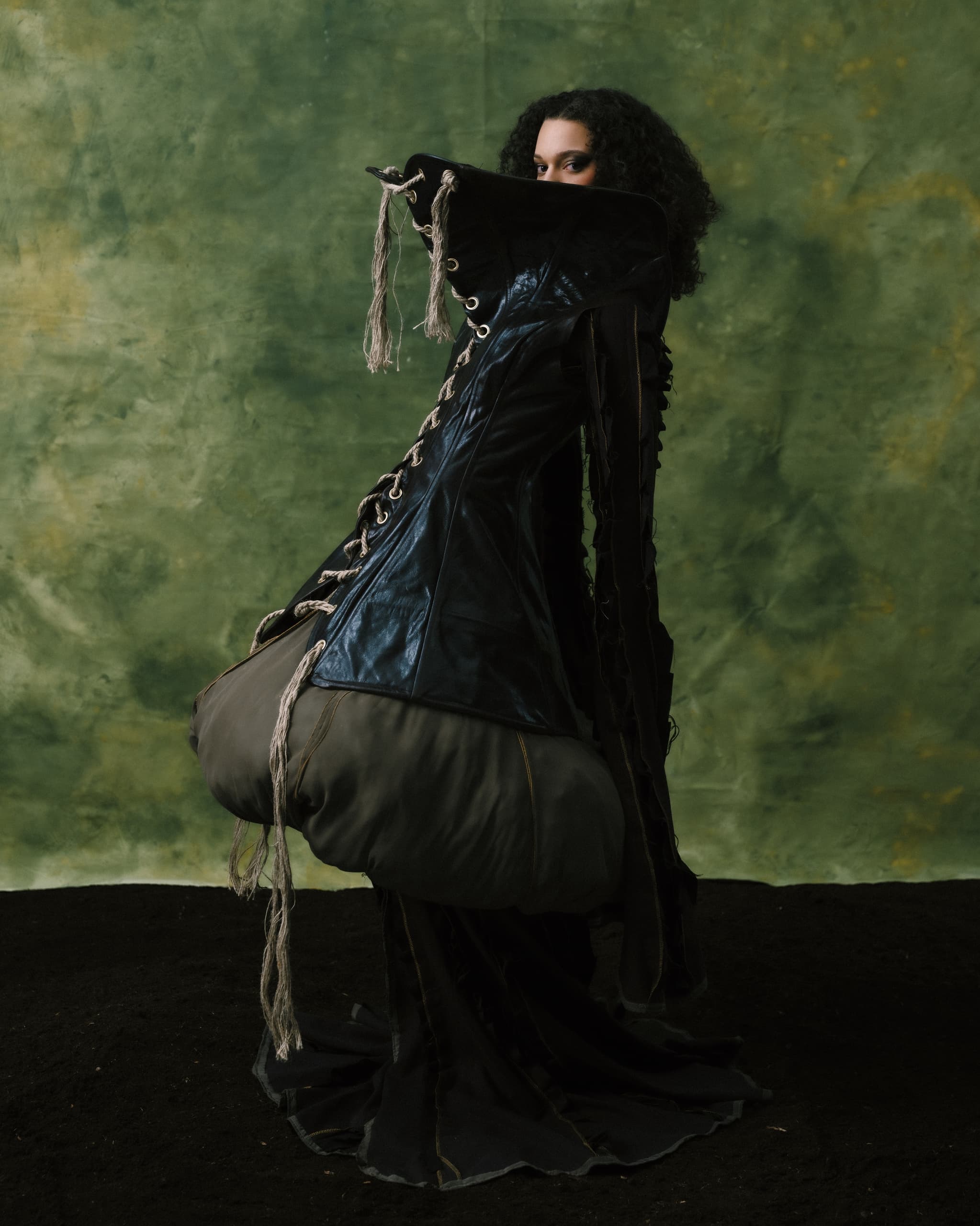 Person in avant-garde fashion against a green backdrop.