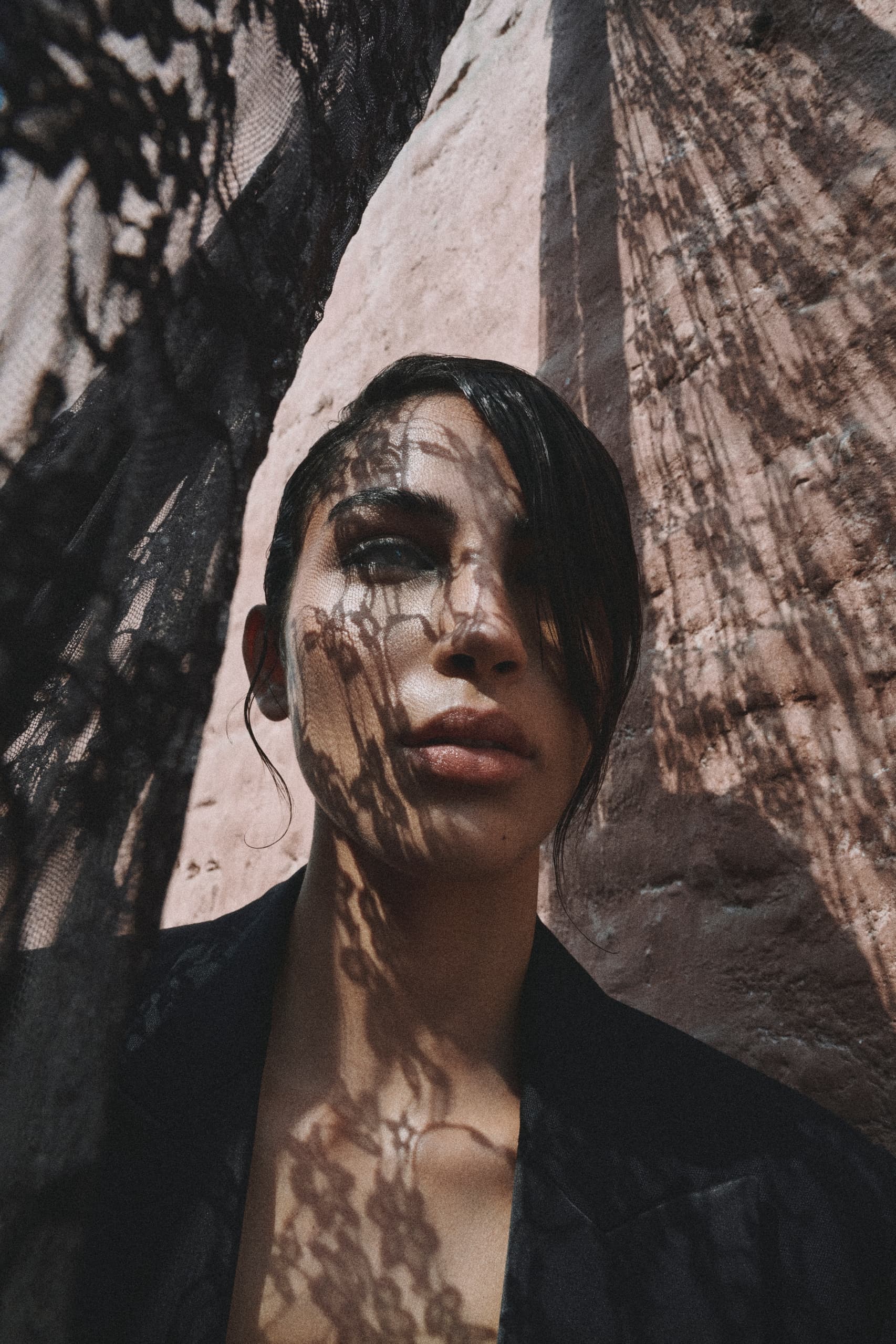 Woman with lace shadow on face against textured wall background.