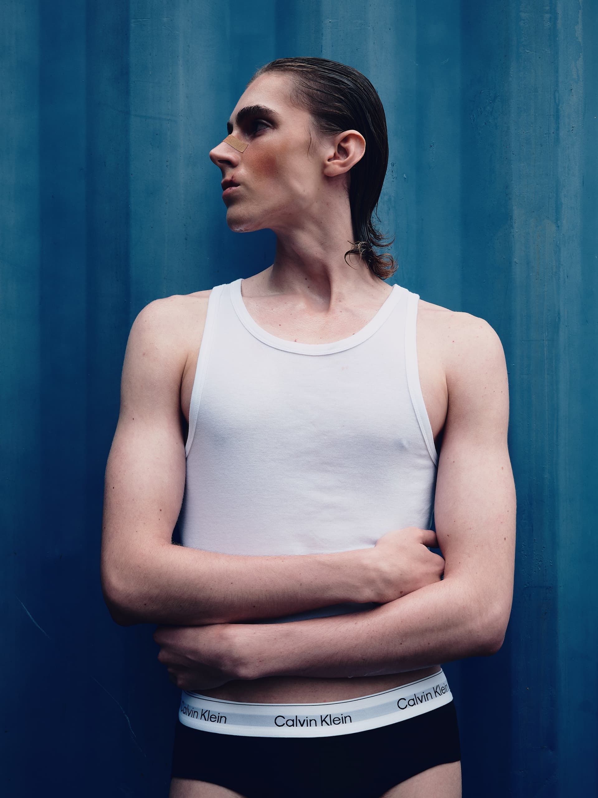 Person wearing a white tank top and underwear against a blue background.