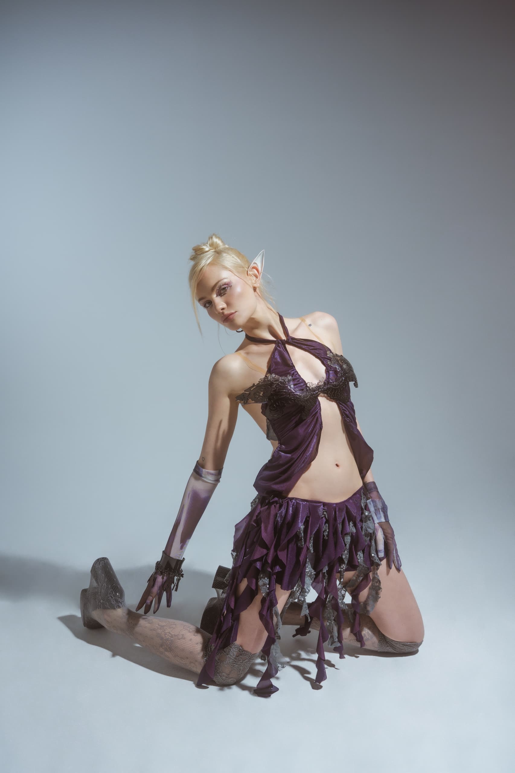 Fantasy elf in purple costume kneeling gracefully with pointed ears and mystical attire.