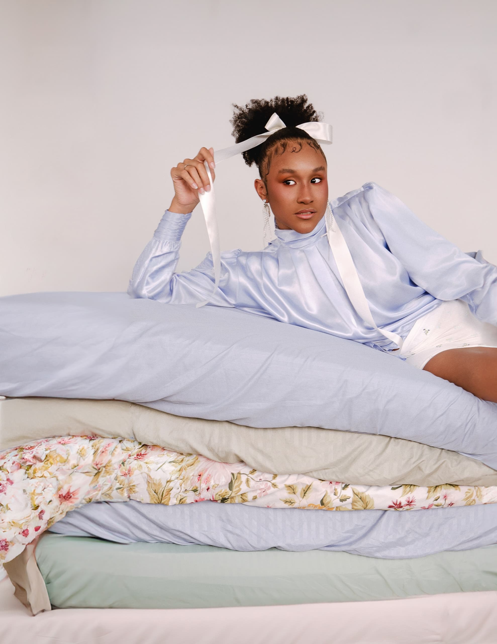 Person in a light blue blouse reclining on layered mattresses, holding a ribbon.