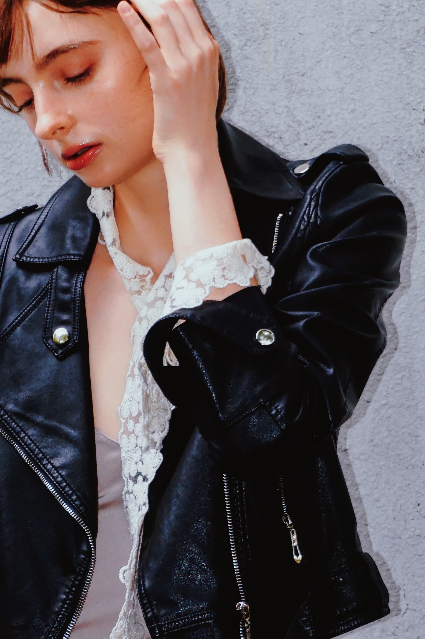 Woman in black leather jacket with lace detail, against a gray background.