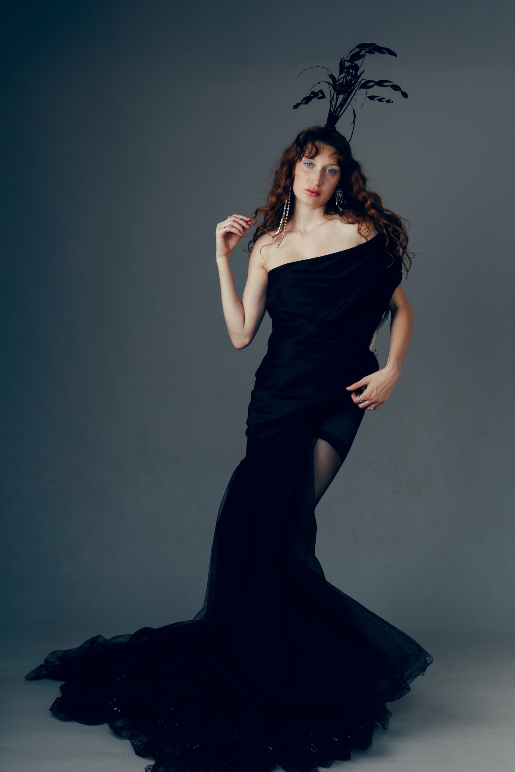 Woman in elegant black gown with feather headpiece, striking a stylish pose.