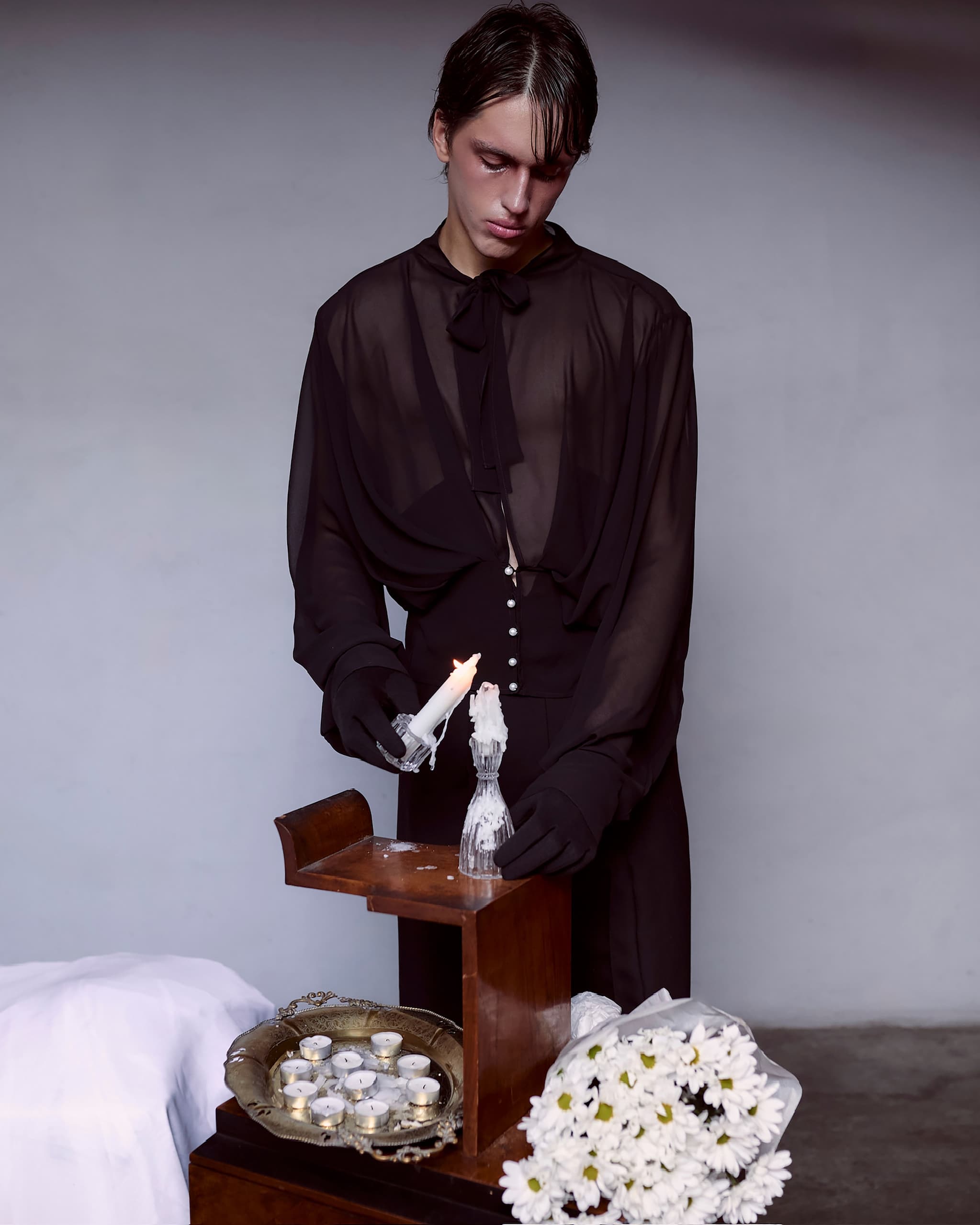 Person lighting a candle near flowers in a moody setting.