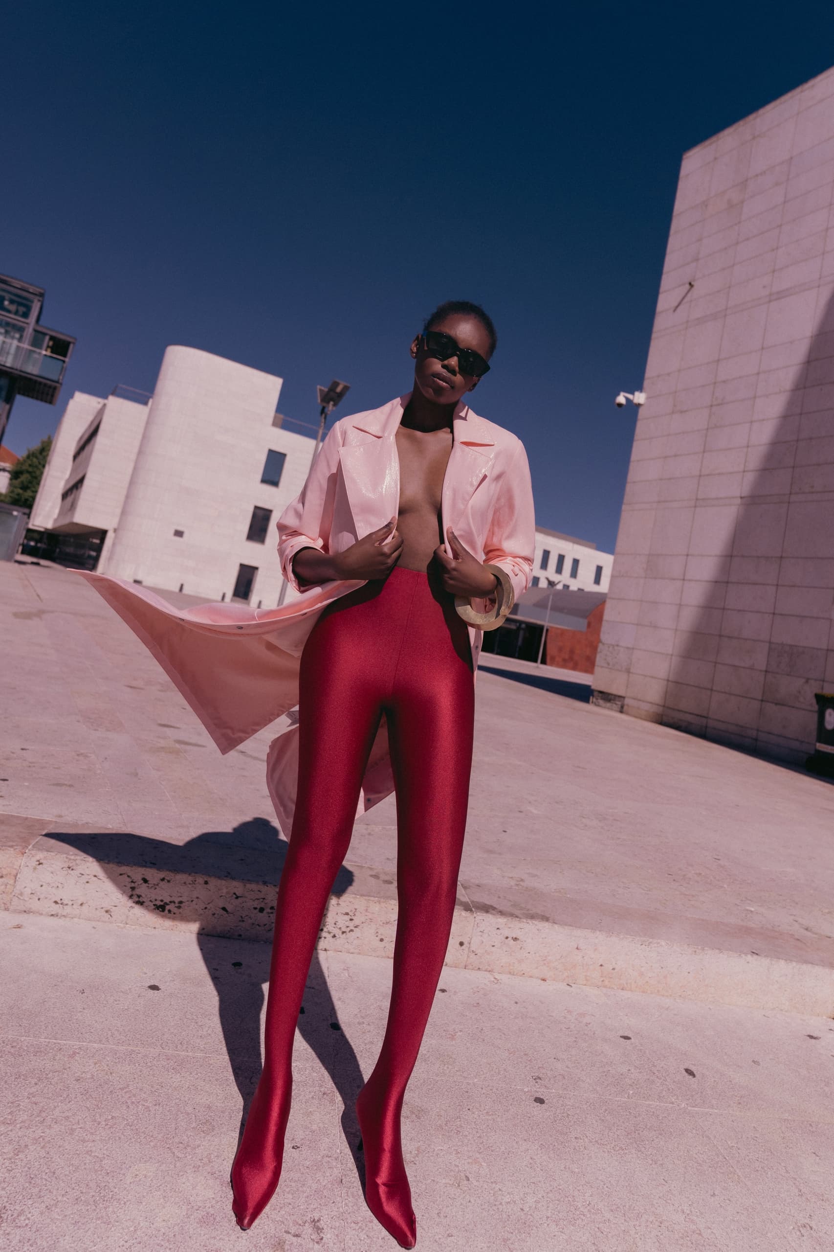 Stylish woman in pink coat and red leggings outdoors.