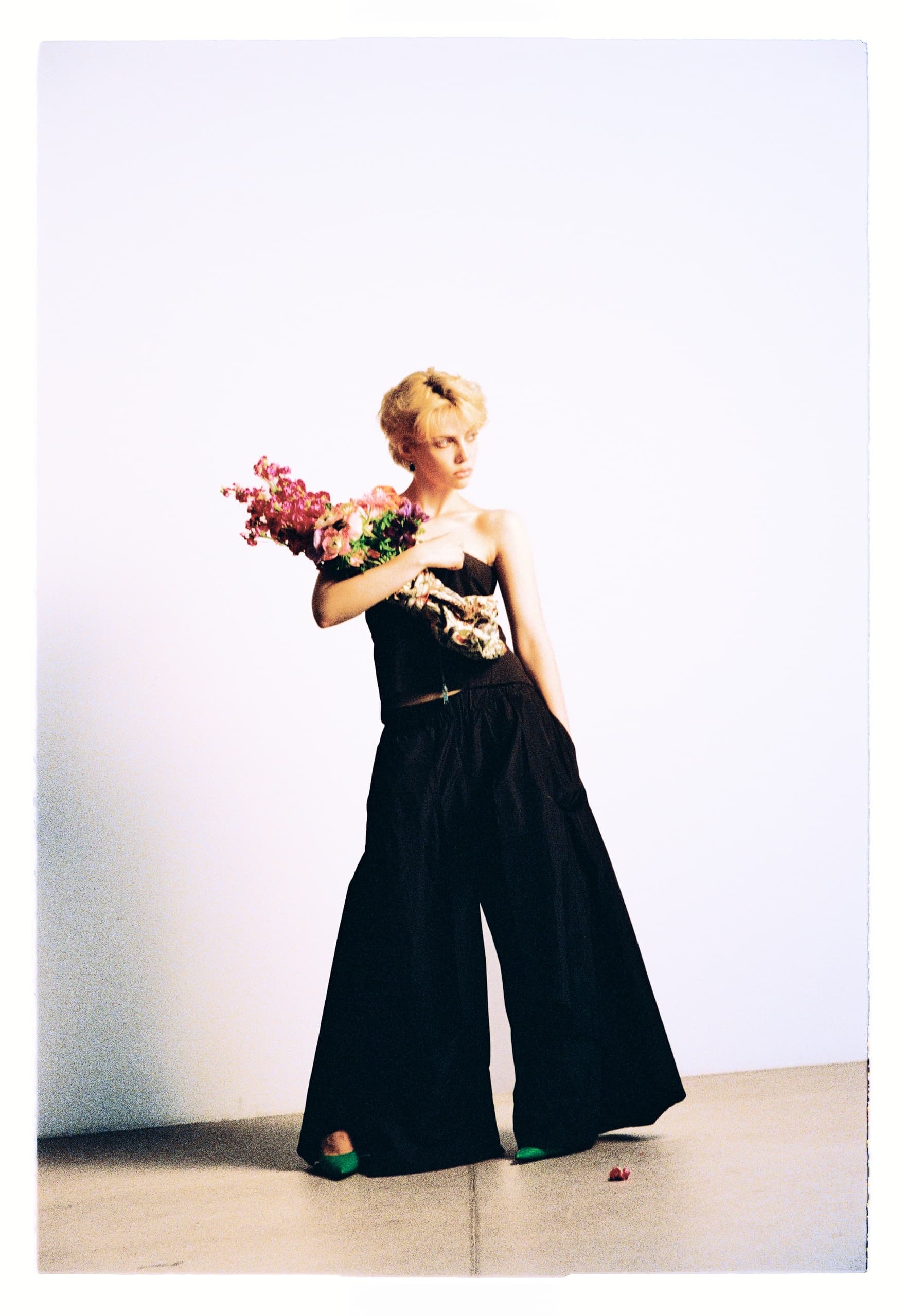 Fashionable person in black outfit holding flowers against a minimalist background.