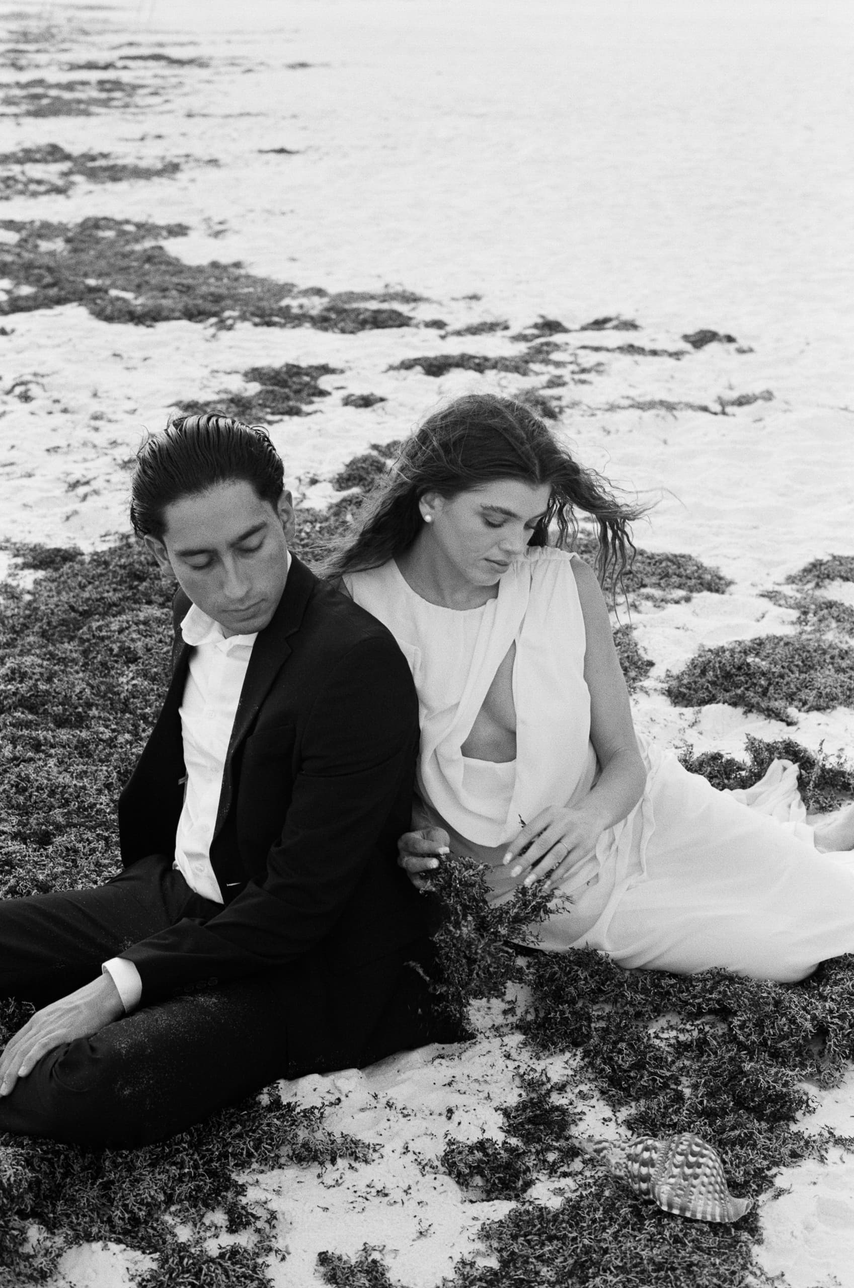 Elegant couple sitting on a sandy beach in black and white.