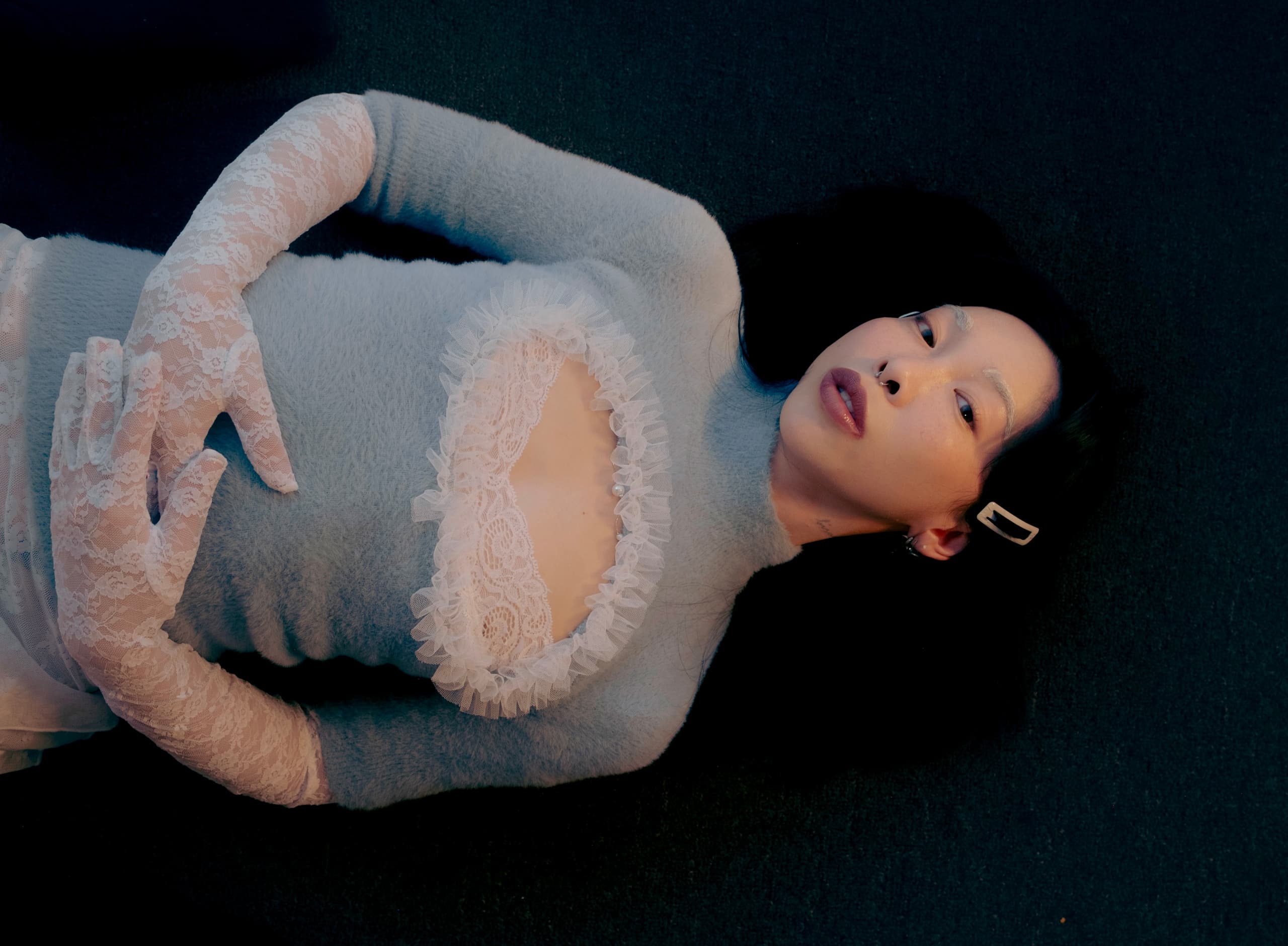 Person in a light blue lace outfit lying on dark surface, elegant and serene pose.