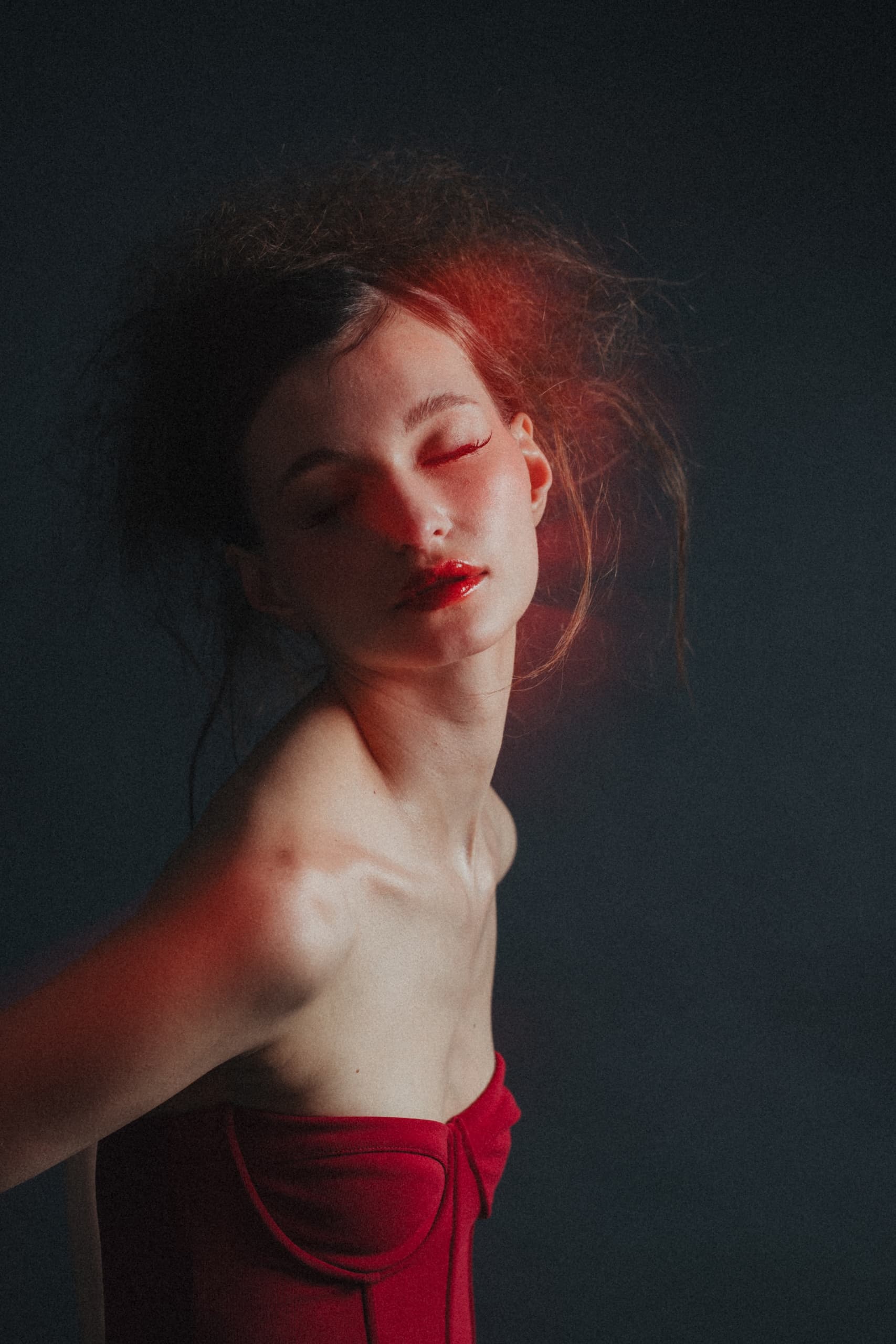 Woman in red dress bathed in red light with dark background, eyes closed.