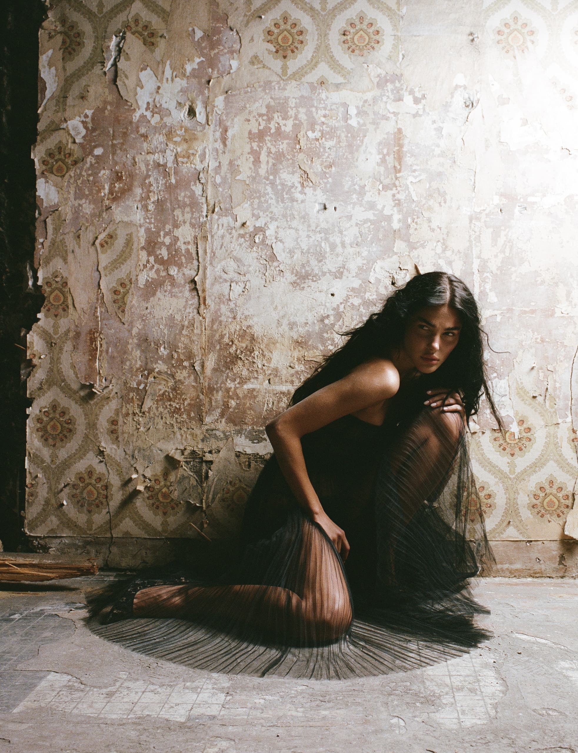 Woman in black dress poses against vintage, distressed wallpaper background.
