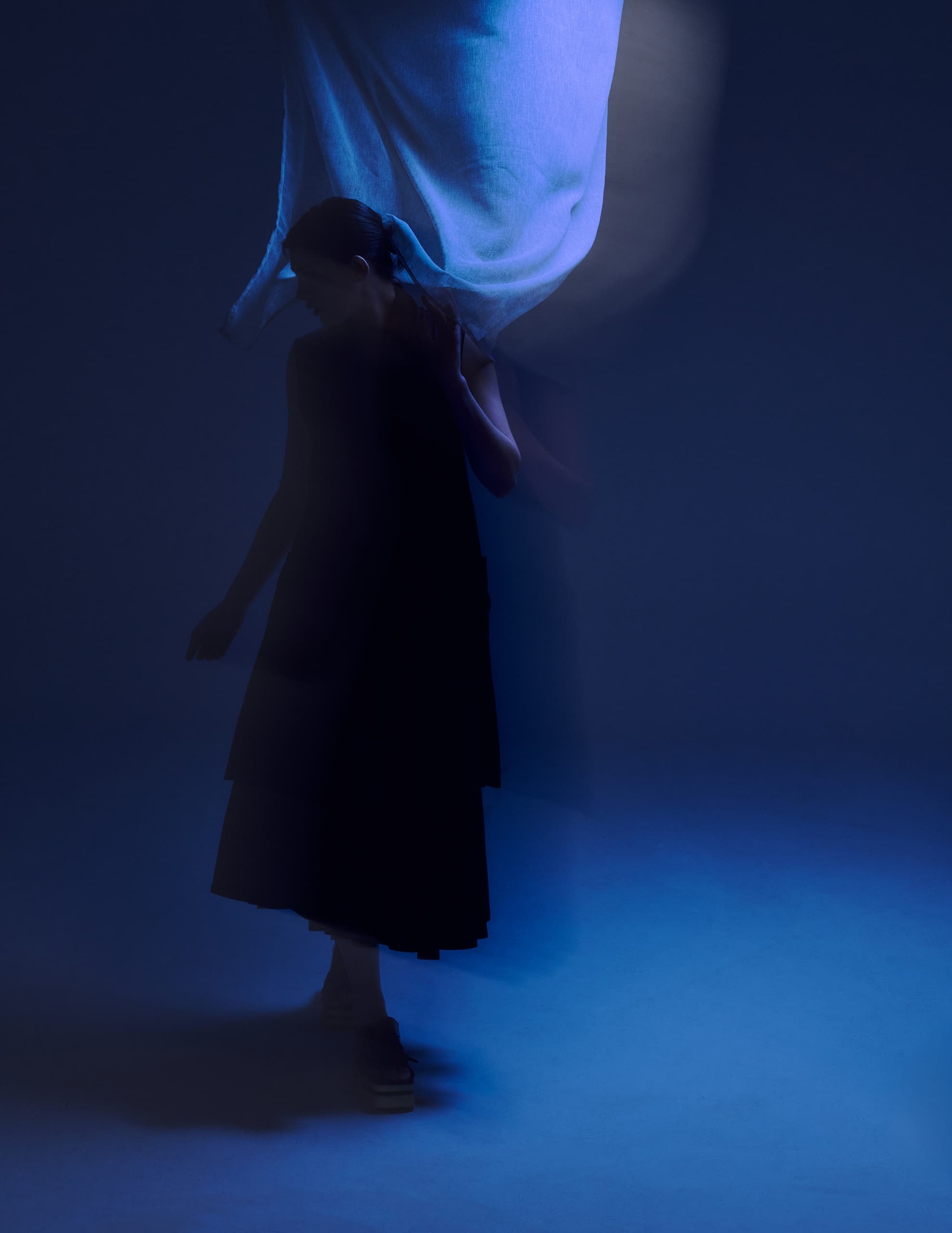 Silhouetted figure in blue ambient light with flowing fabric background.