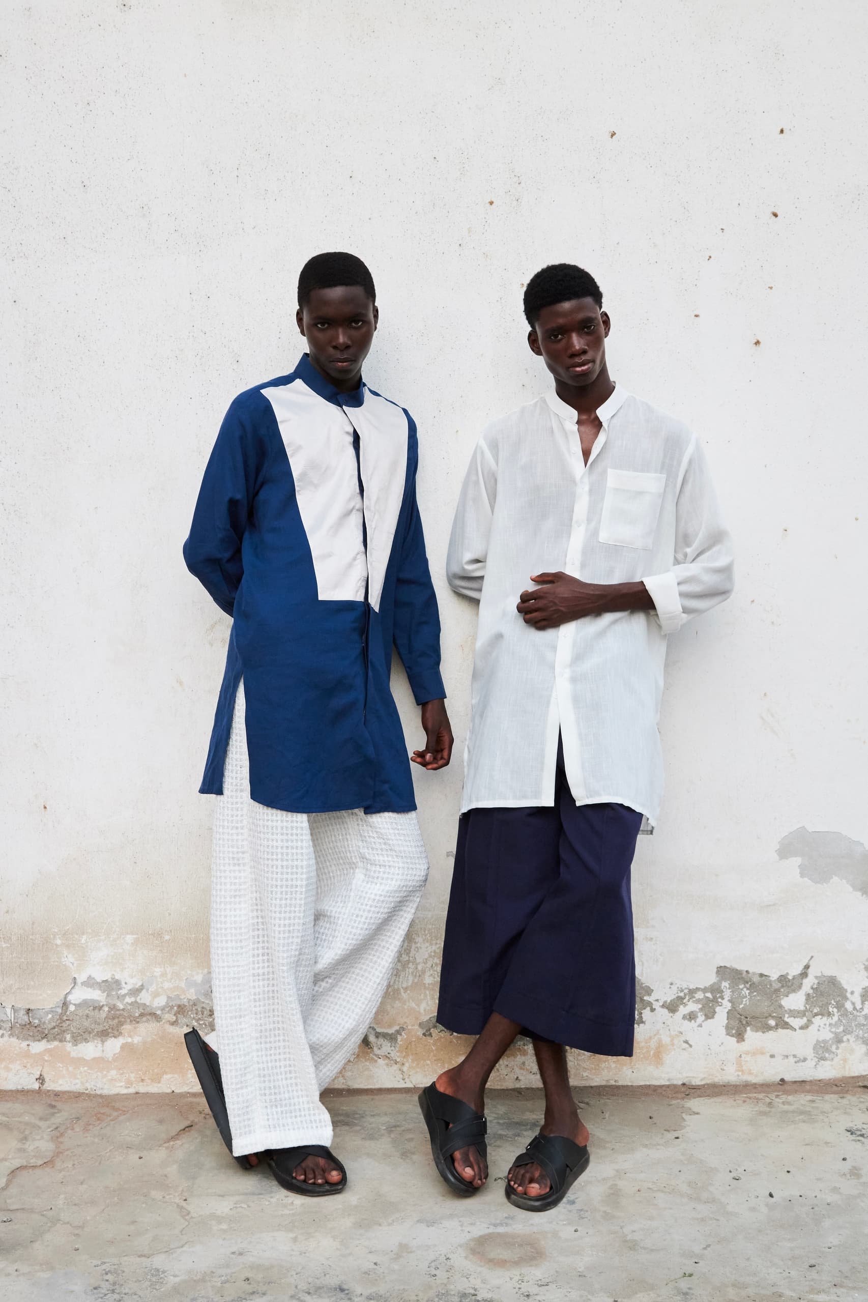 Two models in stylish, contemporary outfits against a minimalist wall backdrop.