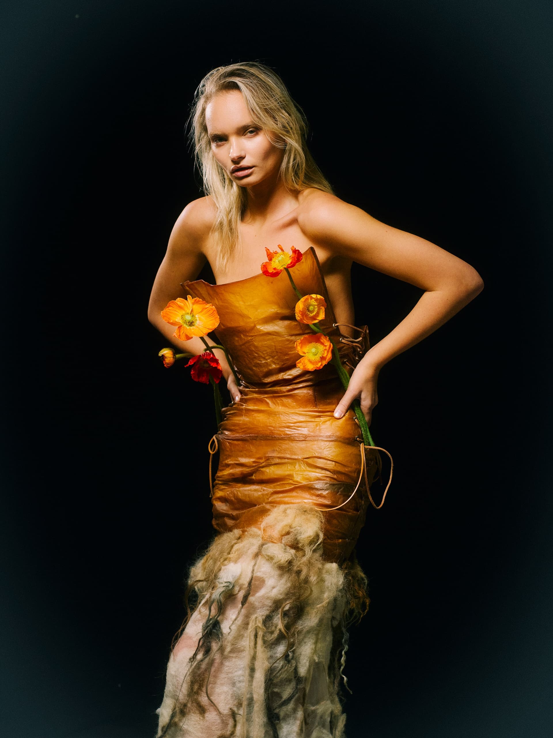 Model in eco-friendly dress with orange flowers, dark background.