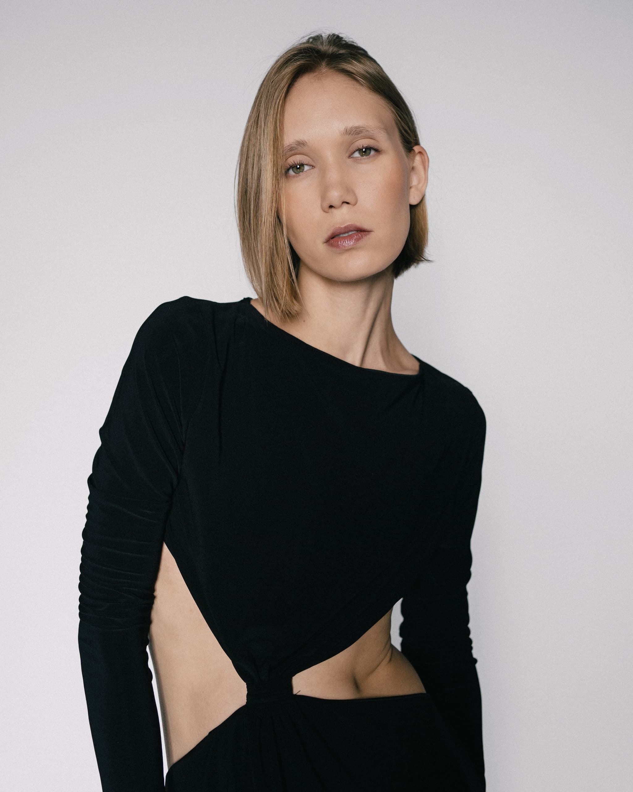 Person in sleek black dress with cutout detail against a neutral background.